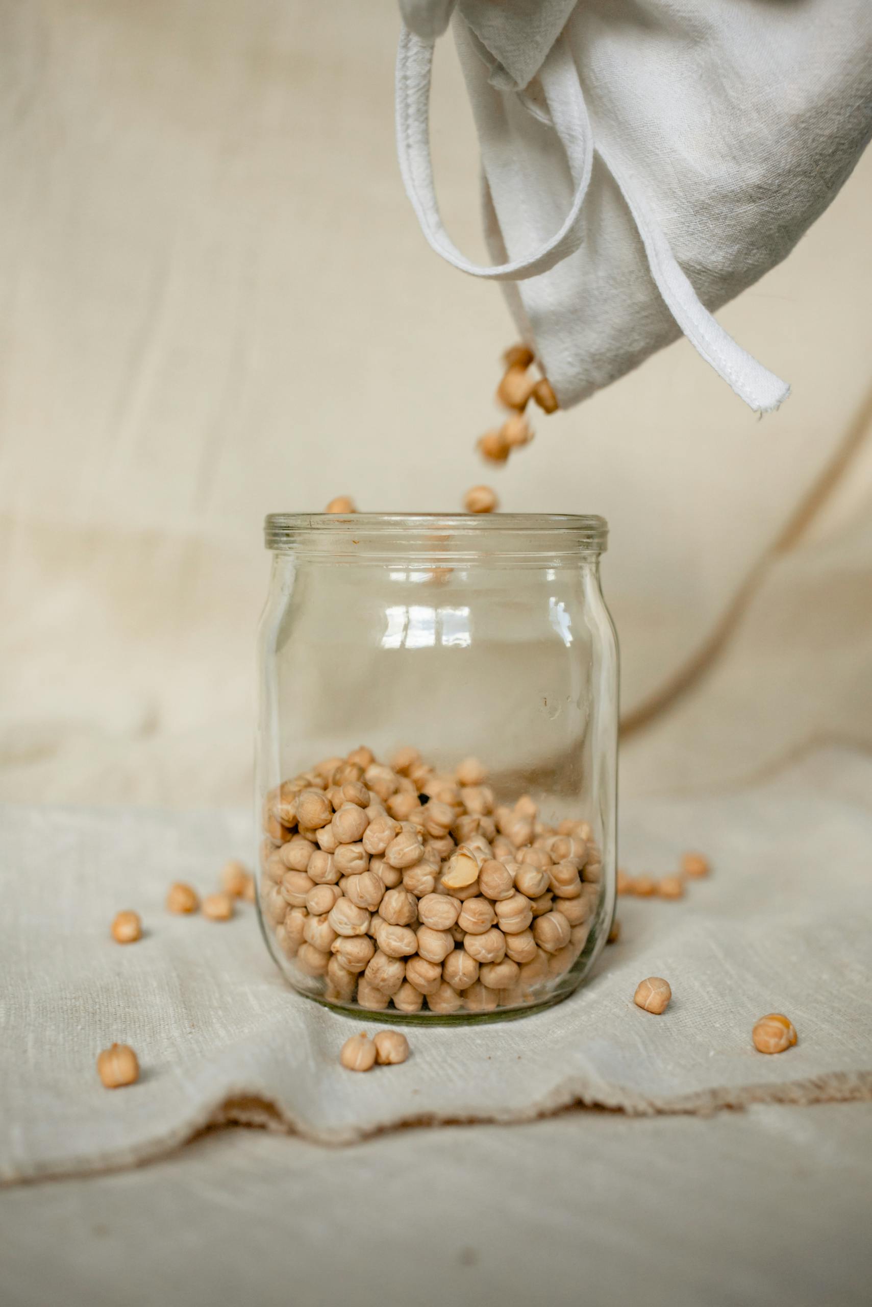 Chickpeas being poured from a cloth bag into a glass jar, showcasing sustainability.