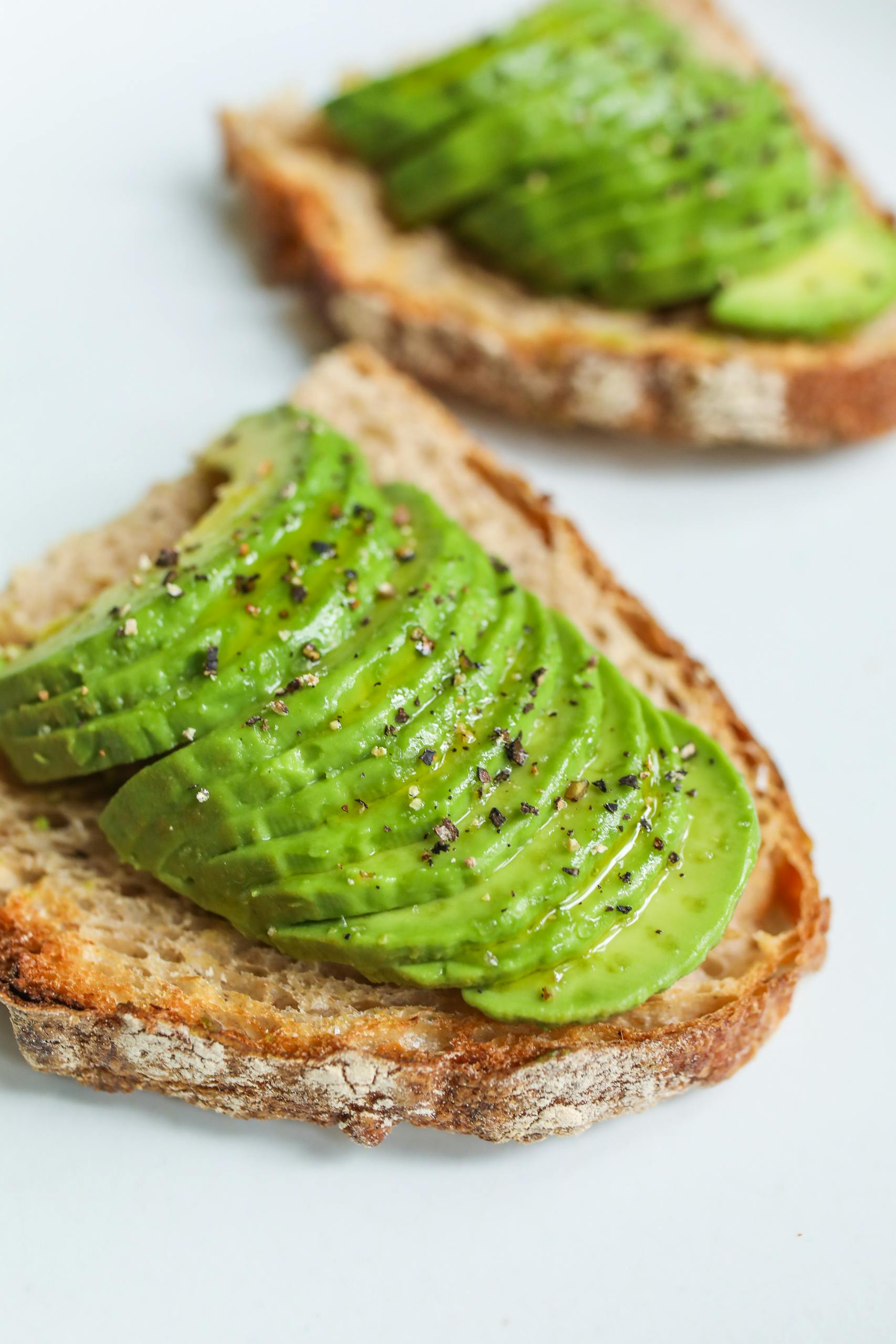 healthy fats: Sliced avocado atop sourdough bread, seasoned with pepper, photographed for a food photography series.