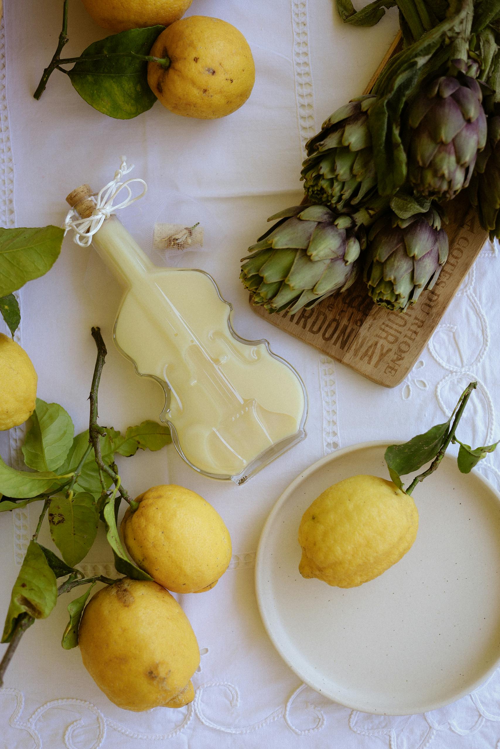 immune-boosting foods: Top view of fresh lemons, artichokes, and decorative violin bottle on a table.