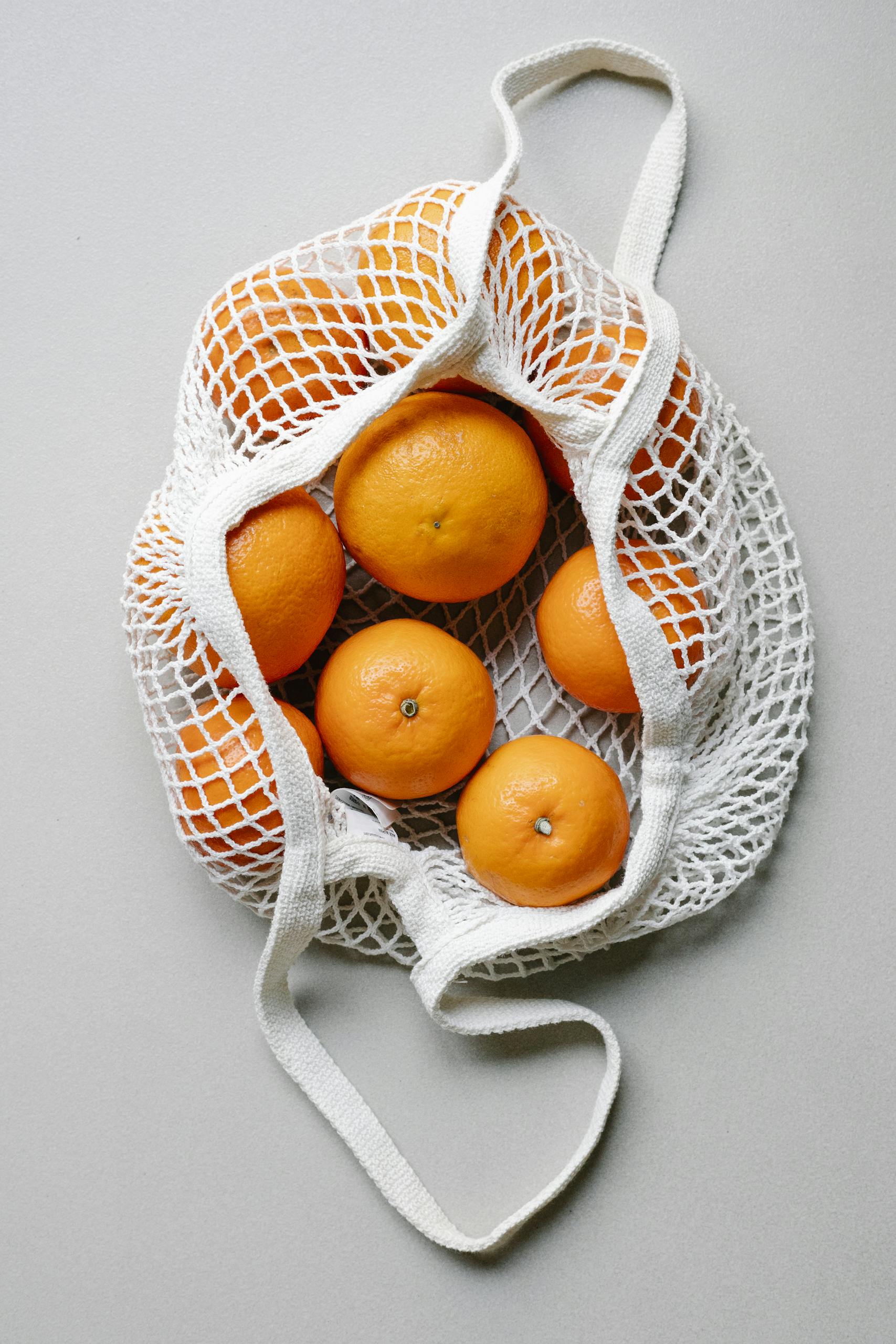 grocery shopping tips: Top view of fresh oranges placed in white eco friendly string bag on white surface