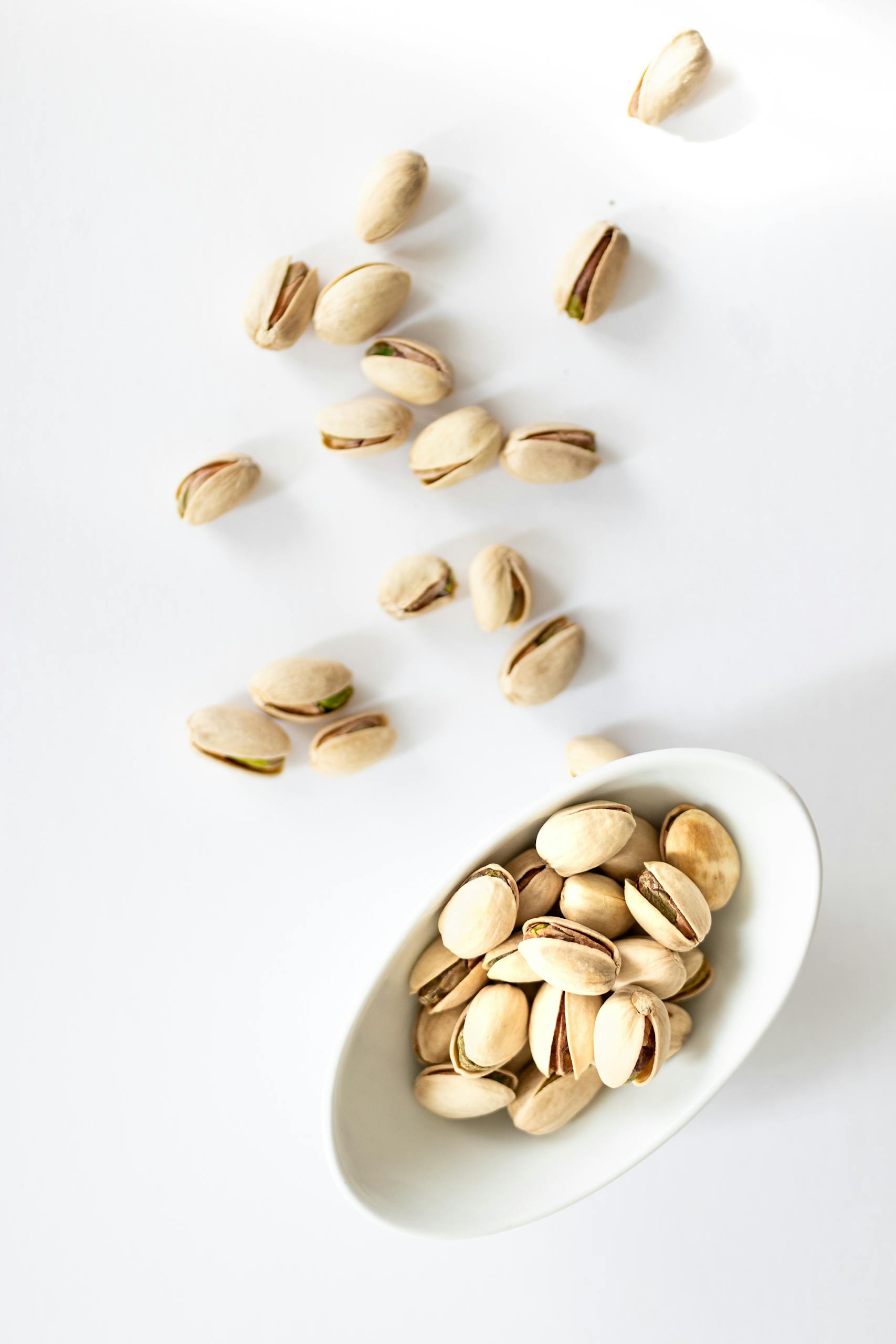 tips for vegetarians: Pistachio nuts in a white bowl on a white background, top view.