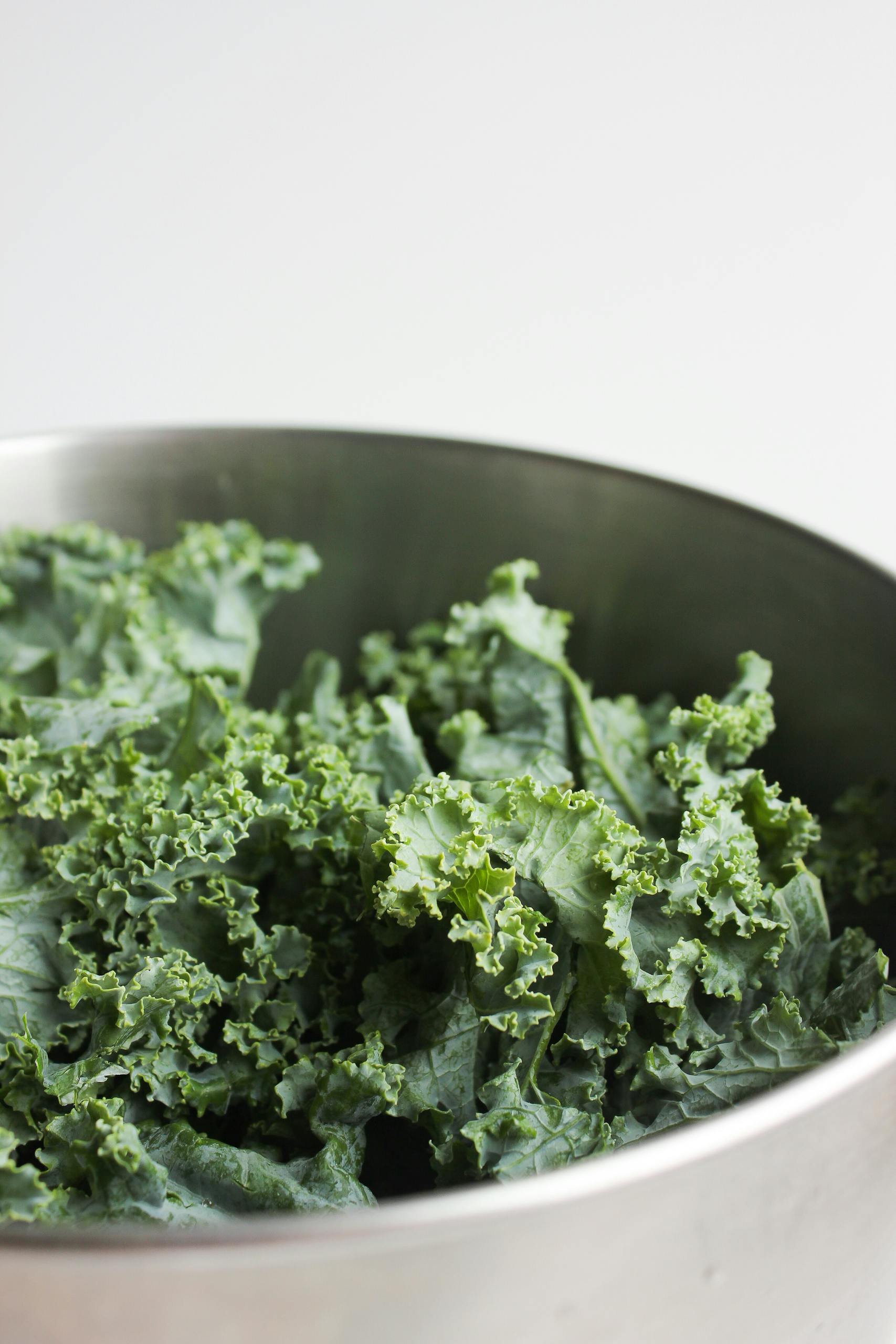 best foods for hormone balance: Fresh green kale leaves displayed in a shiny metal bowl, showcasing their natural texture.