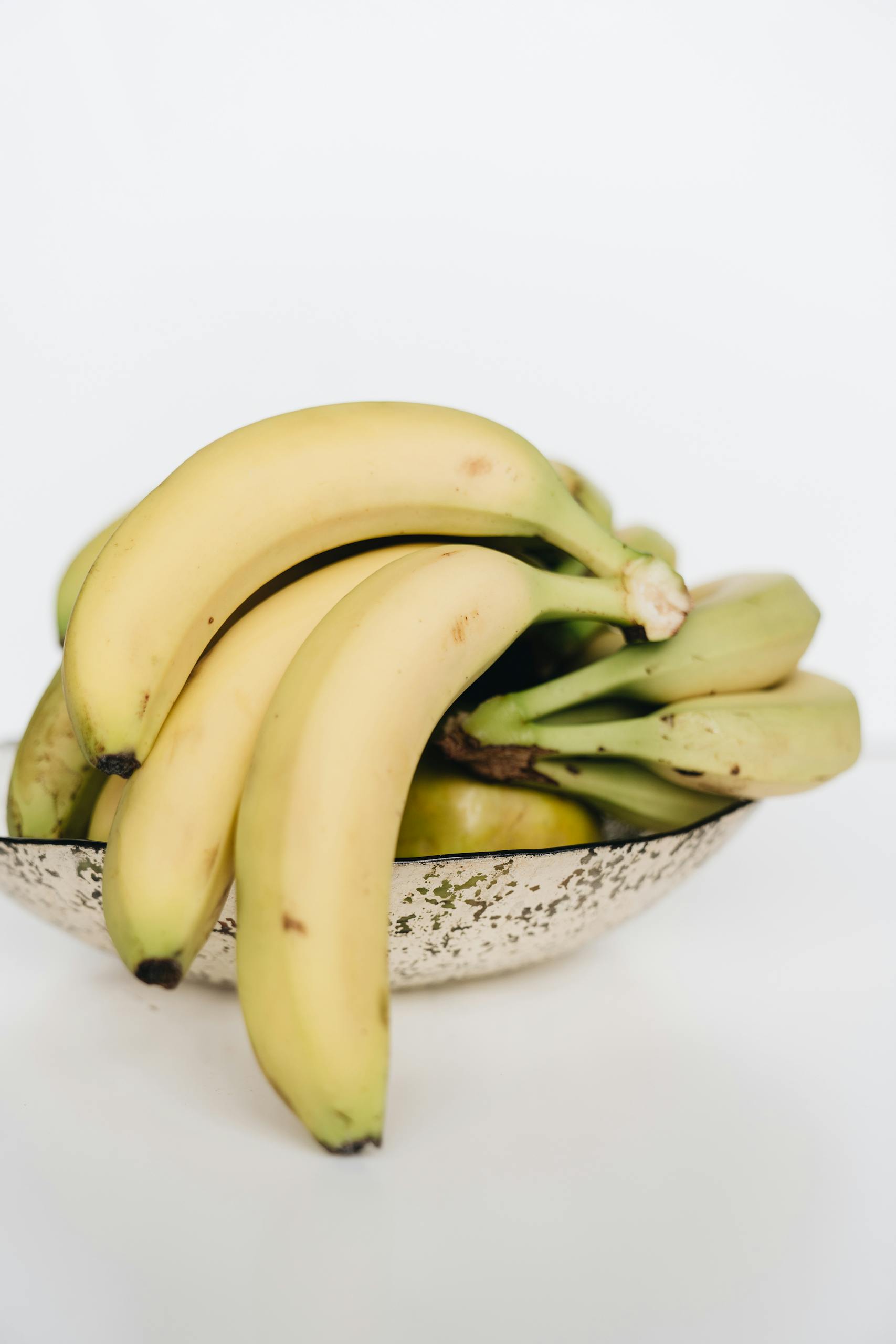 potassium-rich foods for blood pressure: A bunch of ripe bananas elegantly arranged in a speckled bowl on a white background.