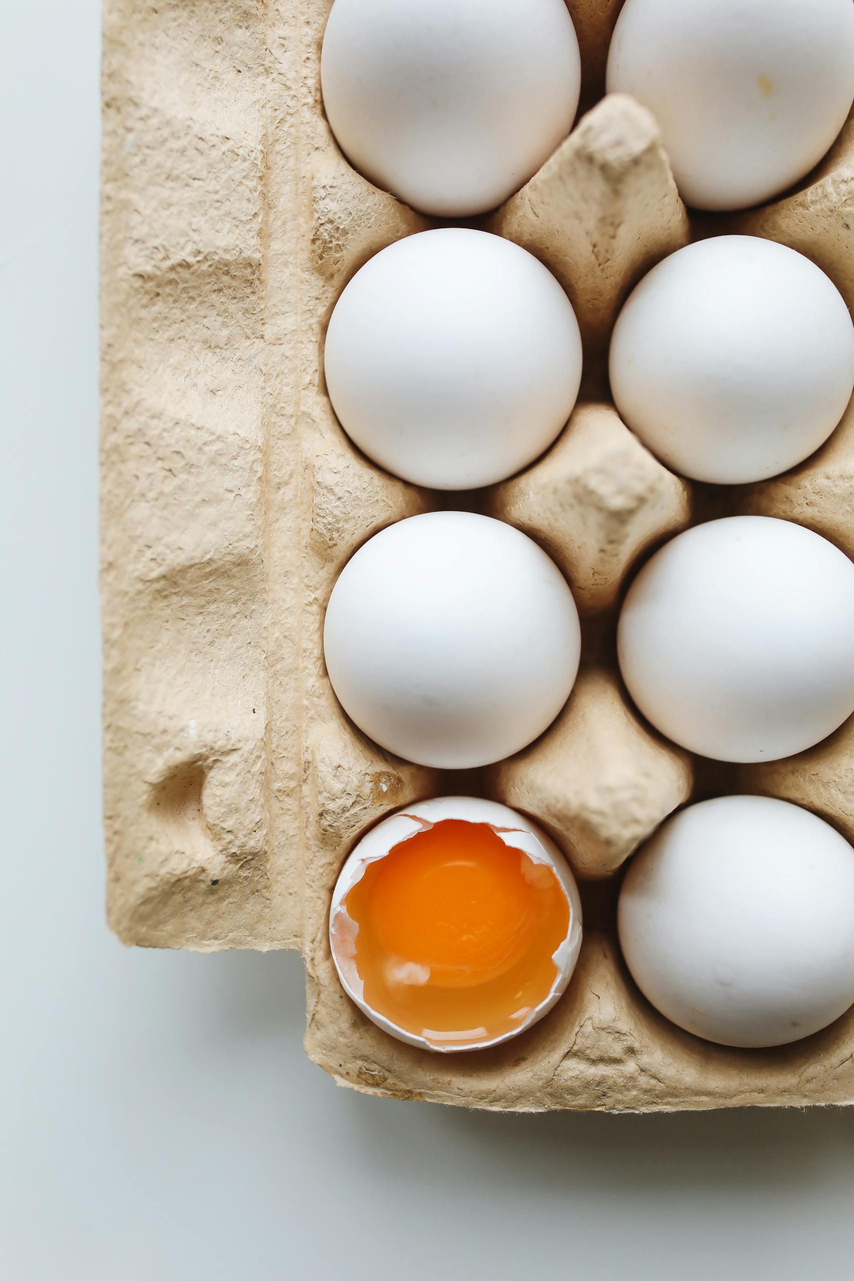 do GLP-1s cause muscle loss? A carton of white eggs with one cracked, revealing vibrant yolk. Ideal for food and health themes.