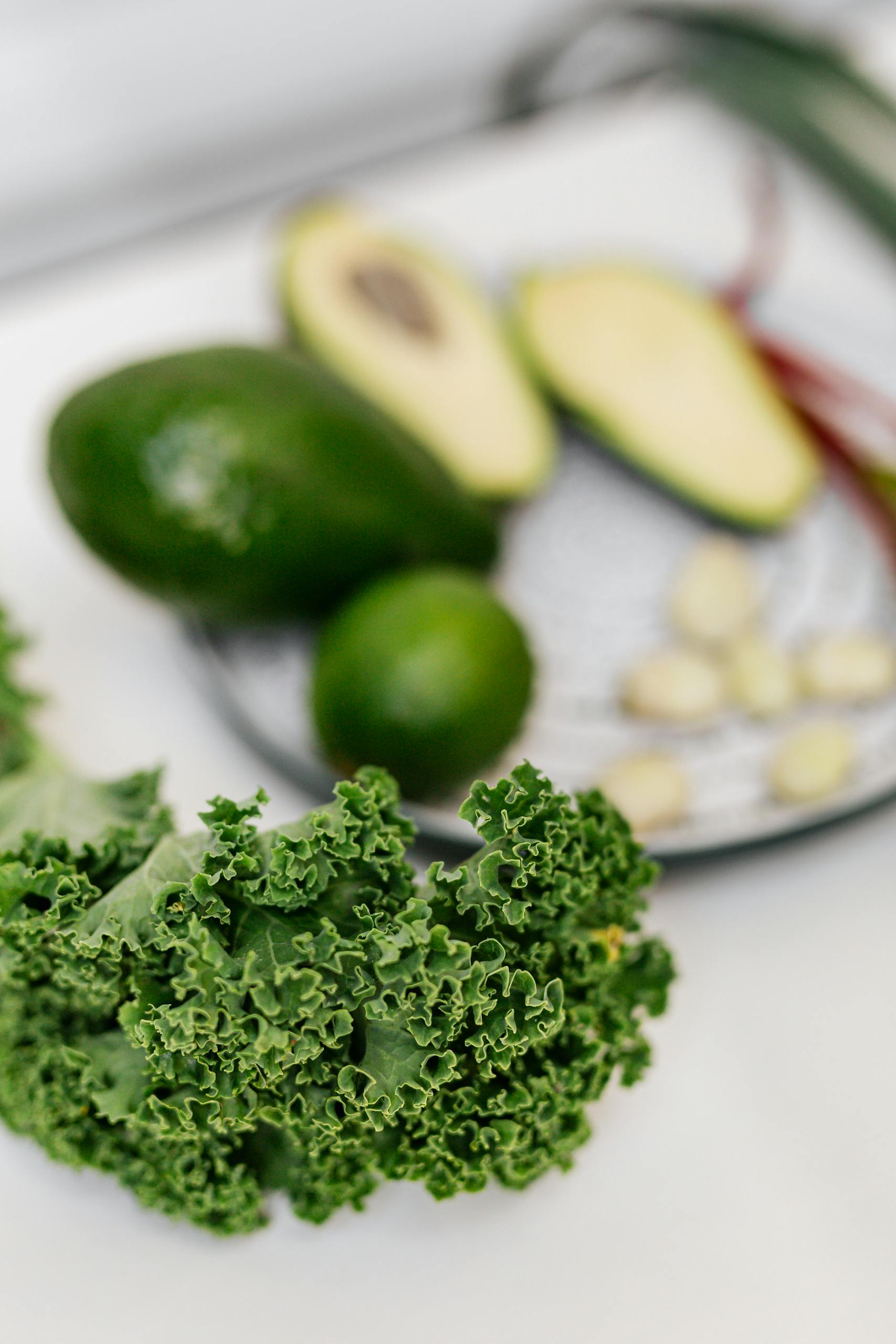 best foods to reduce brain fog: A close-up of fresh kale with avocado, lime, and garlic on a white surface.