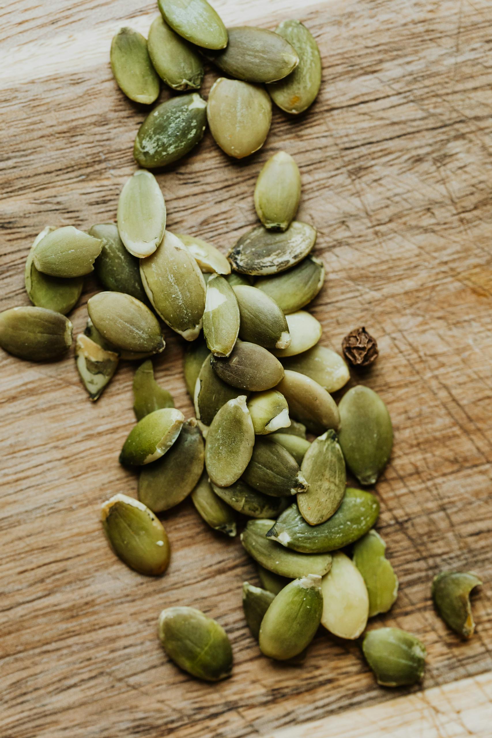 Foods That Help With PMS Symptoms: A detailed shot of green pumpkin seeds scattered on a wooden board, perfect for food blogs or healthy lifestyle concepts.