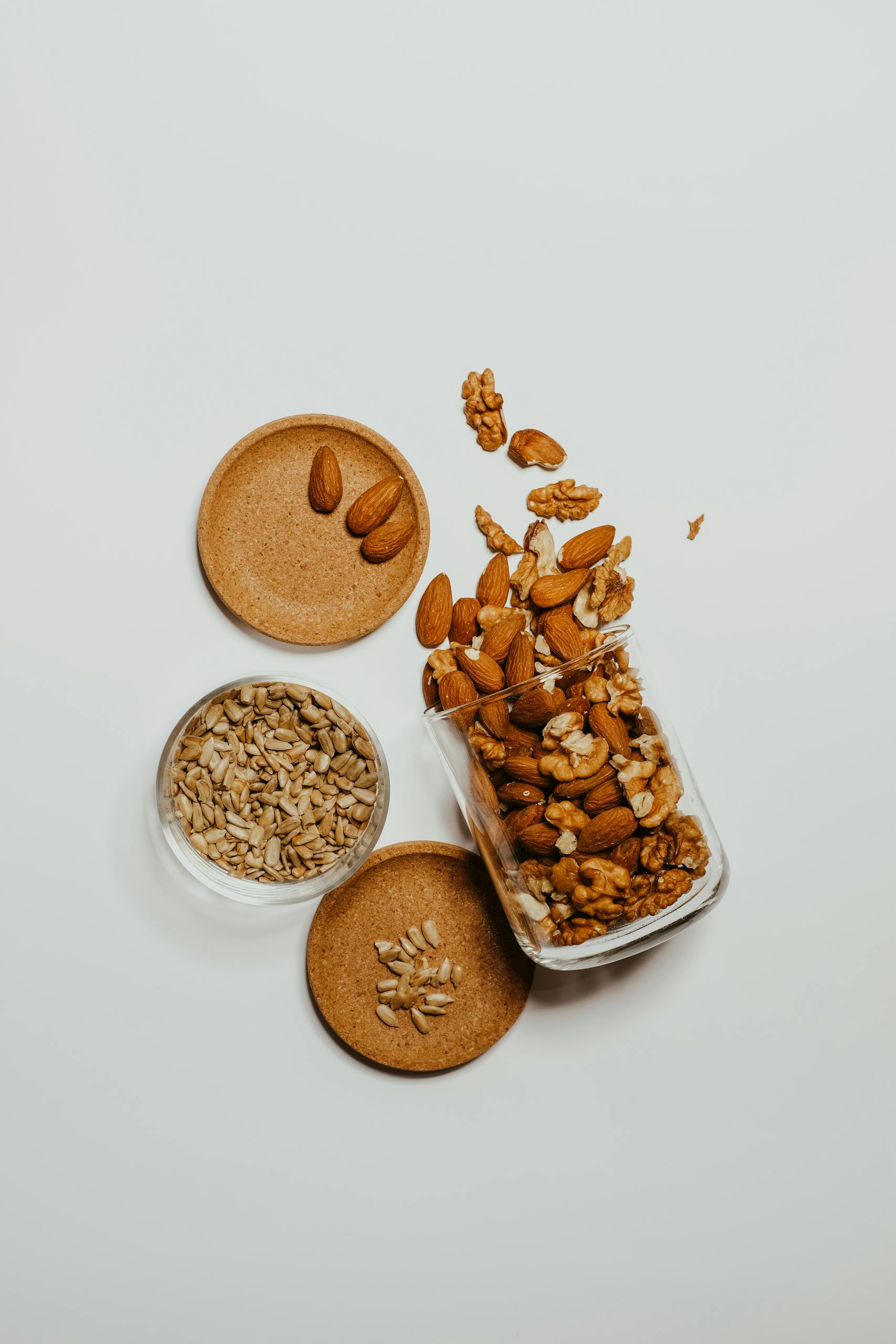 best healthy snacks at whole foods market: A flat-lay of mixed almonds, walnuts, and sunflower seeds in glass jars over a white surface.