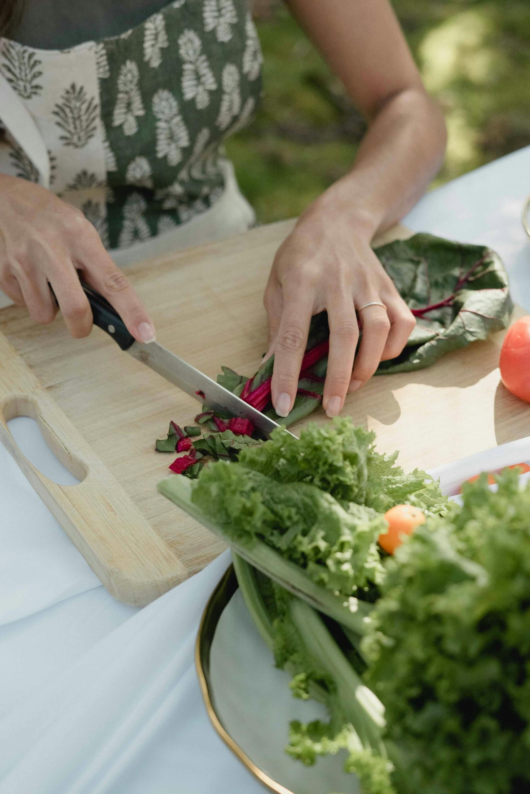 Swiss chard benefits: A person slicing swiss chard on a chopping board outdoors, surrounded by fresh vegetables.