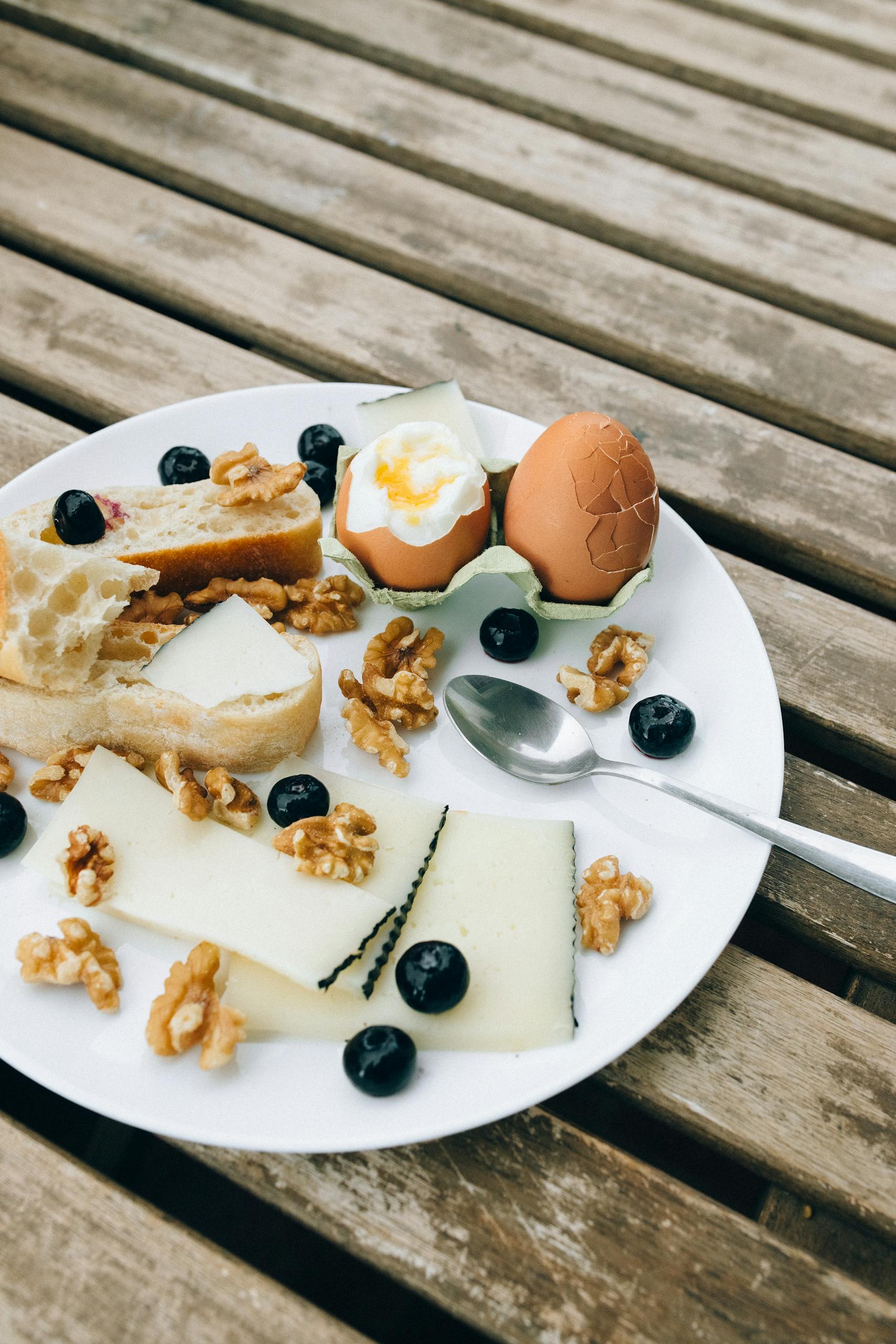 high-protein snacks: A rustic breakfast plate with cheese, walnuts, eggs, and blueberries on a wooden table.