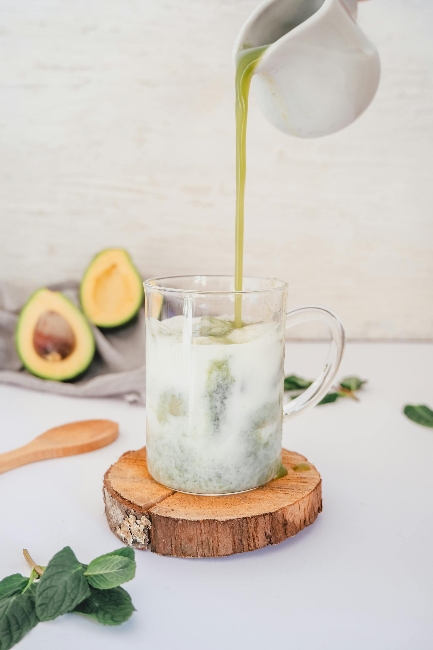 best foods for gut health: Close-up of an avocado smoothie with matcha being poured in a clear glass, surrounded by avocados.