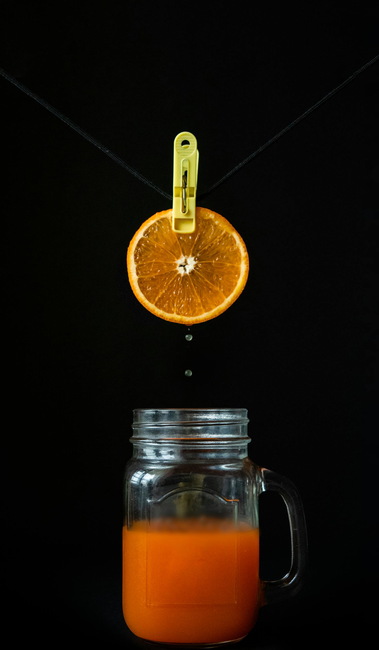 how to make kombucha: Creative shot of an orange slice dripping juice into a jar on a black background.