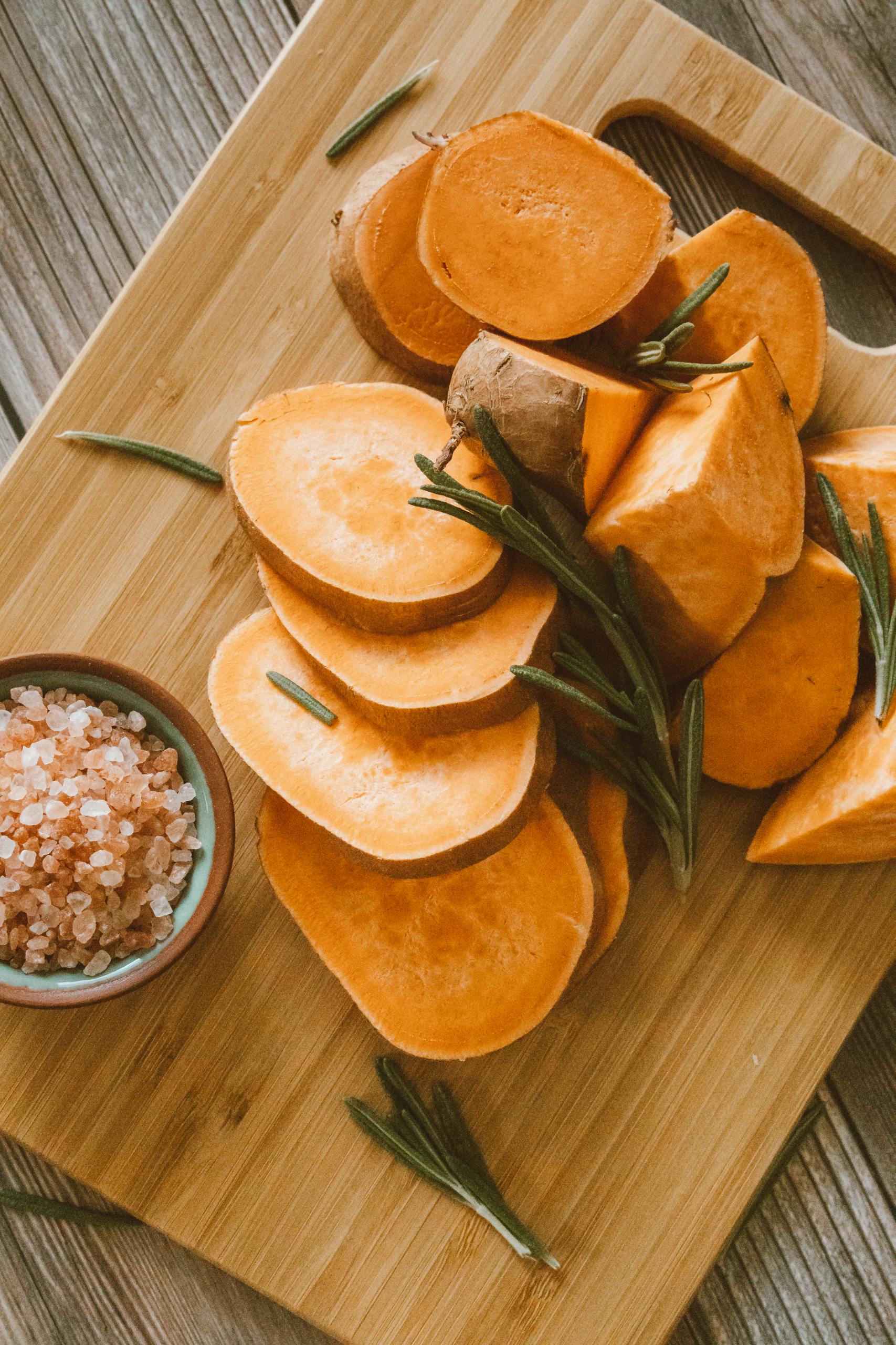 potassium-rich foods for blood pressure: Freshly sliced sweet potatoes on a chopping board with Himalayan salt and rosemary.