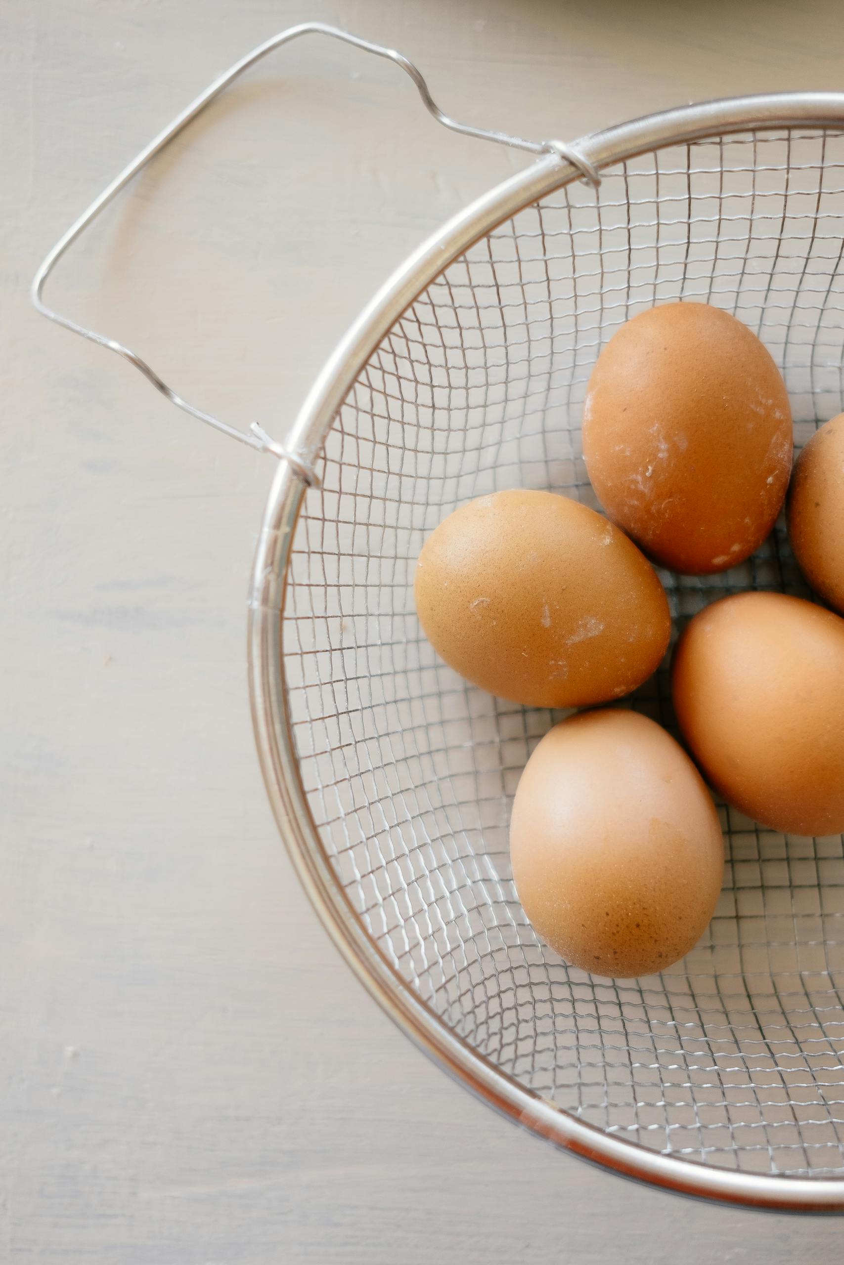 high-protein snacks: A close-up shot of fresh brown eggs in a metal wire basket on a neutral background.