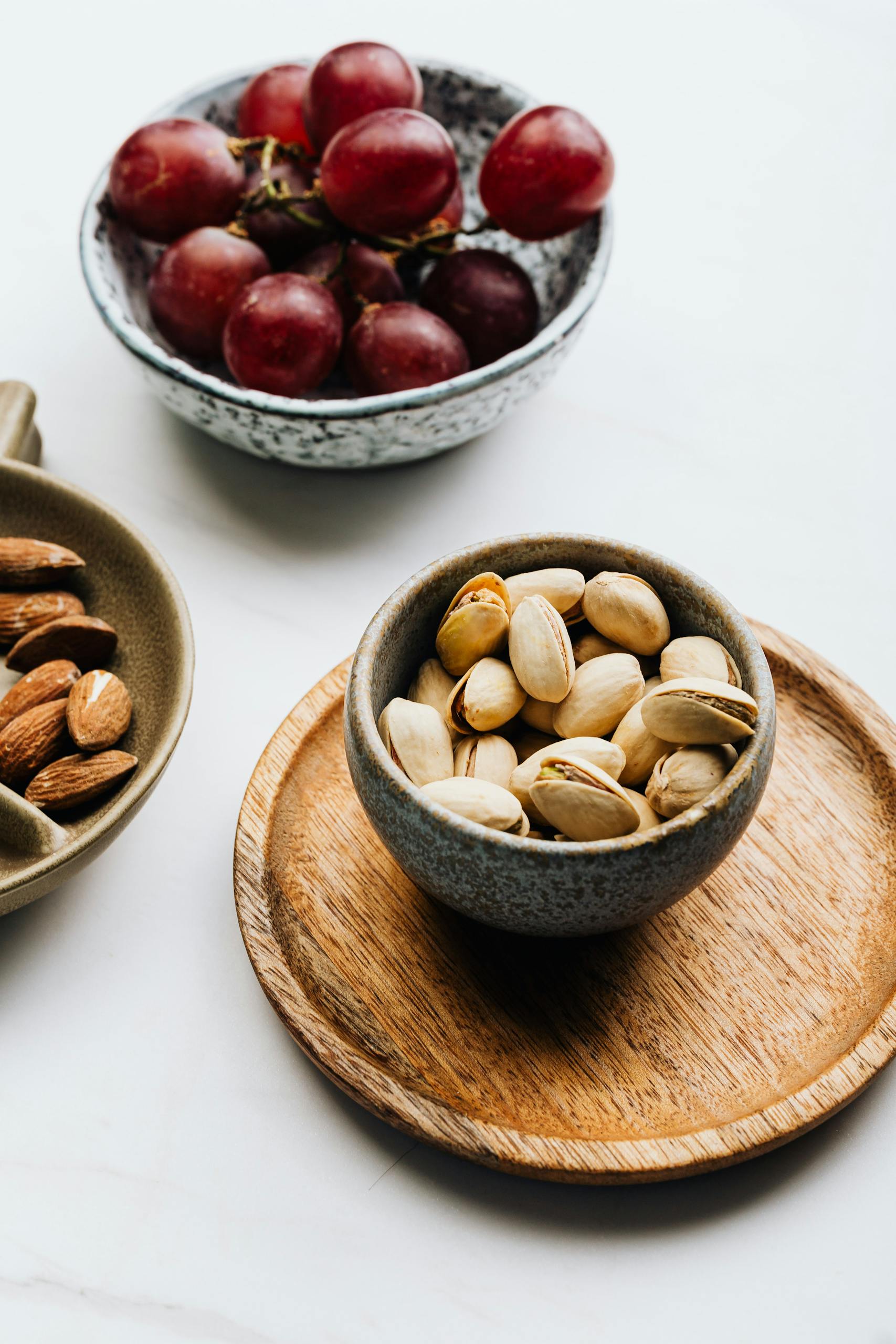 is snacking bad for metabolism: A delicious assortment of pistachios, almonds, and grapes in rustic bowls on a white background.