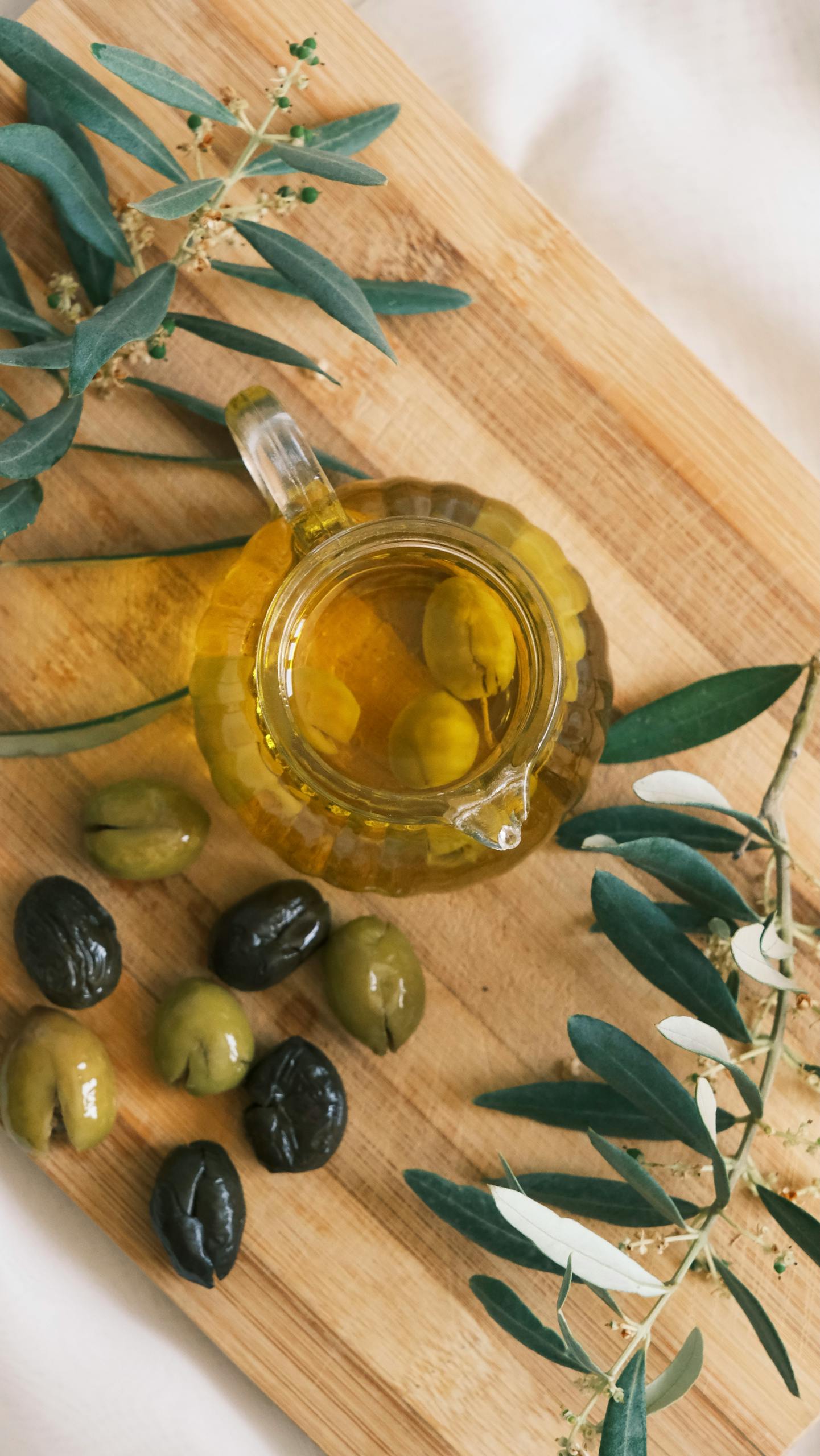 olive oil vs. avocado oil: A top view of a cruet with olive oil and olives on a wooden cutting board.