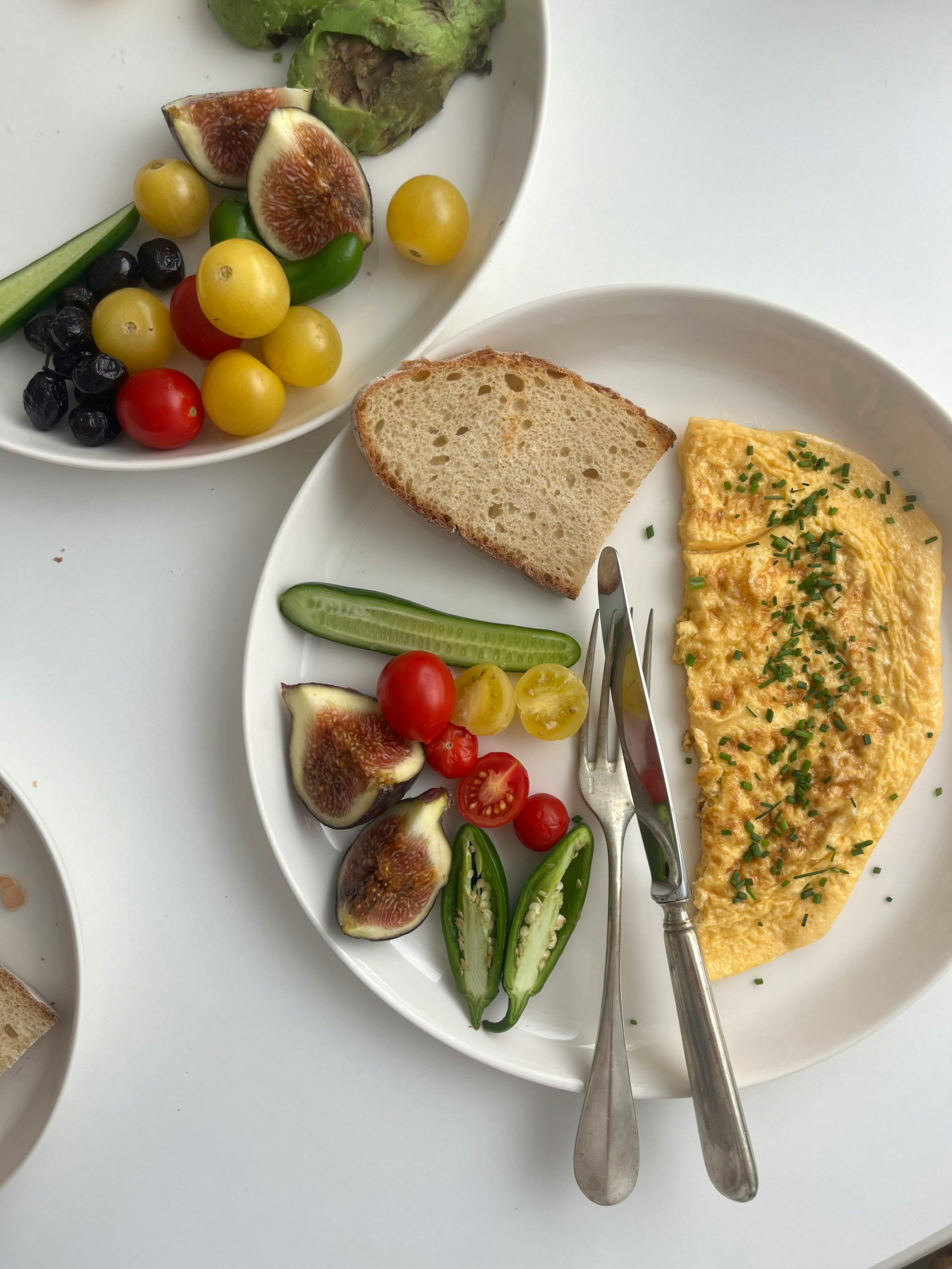 Body recomposition meal plan for beginners: A vibrant breakfast featuring omelette, fresh vegetables, figs, and bread on a white plate.