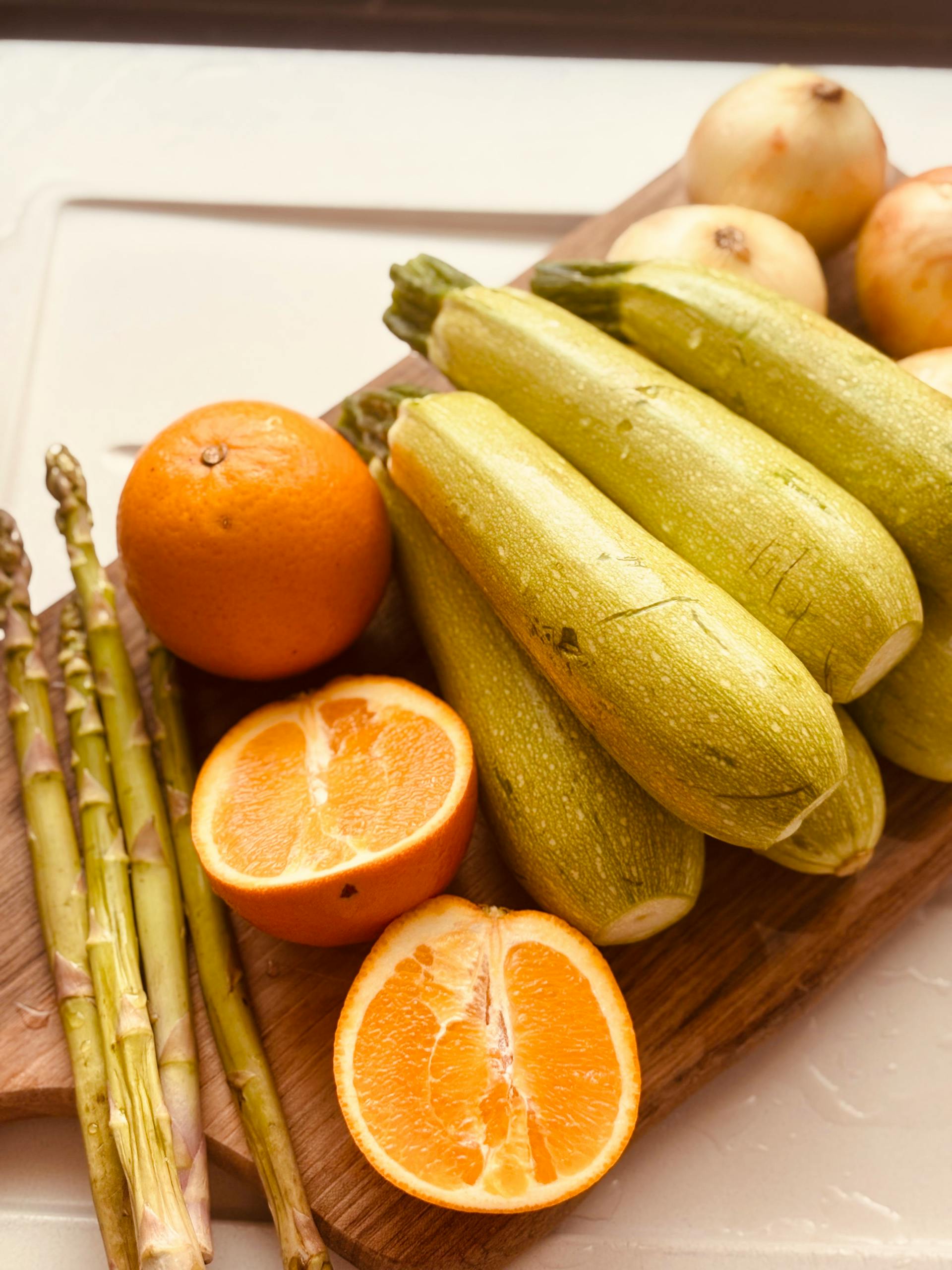 Body recomposition meal plan for beginners: Assorted fresh produce including zucchini, oranges, onions, and asparagus on a wooden board.