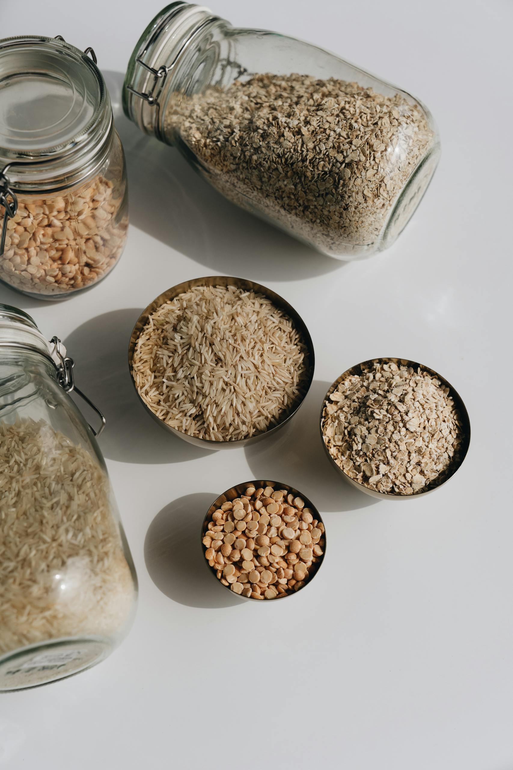 high-protein, high-fiber foods: Assorted grains displayed in bowls and jars on a white surface, emphasizing healthy eating.