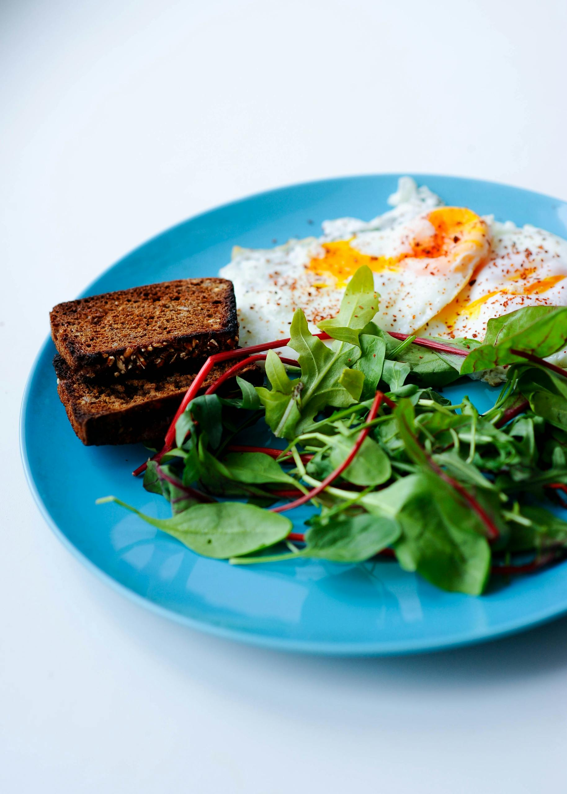Body recomposition meal plan for beginners: Delicious breakfast featuring fried eggs, toast, and fresh greens served on a vibrant blue plate.