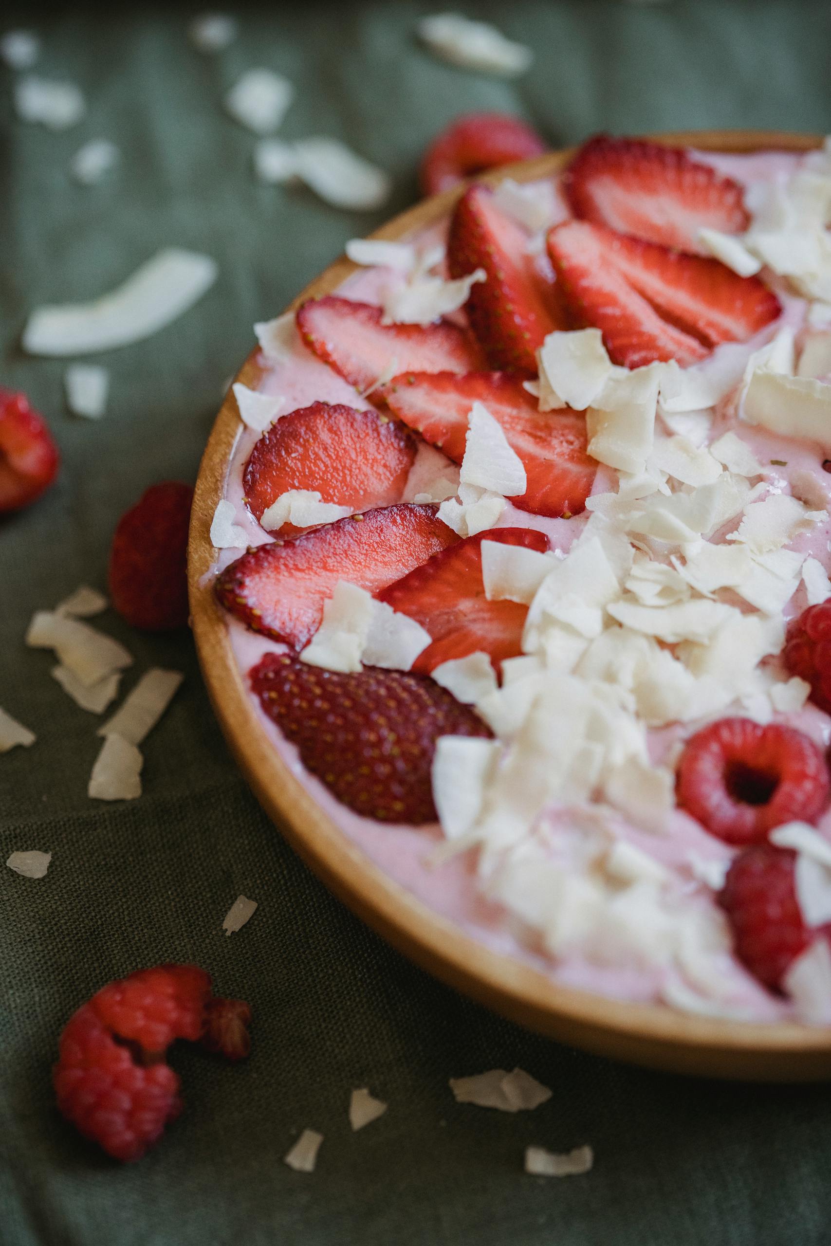 how to eat more fiber without bloating: A delicious strawberry and coconut yogurt bowl topped with fresh raspberries and coconut shavings.