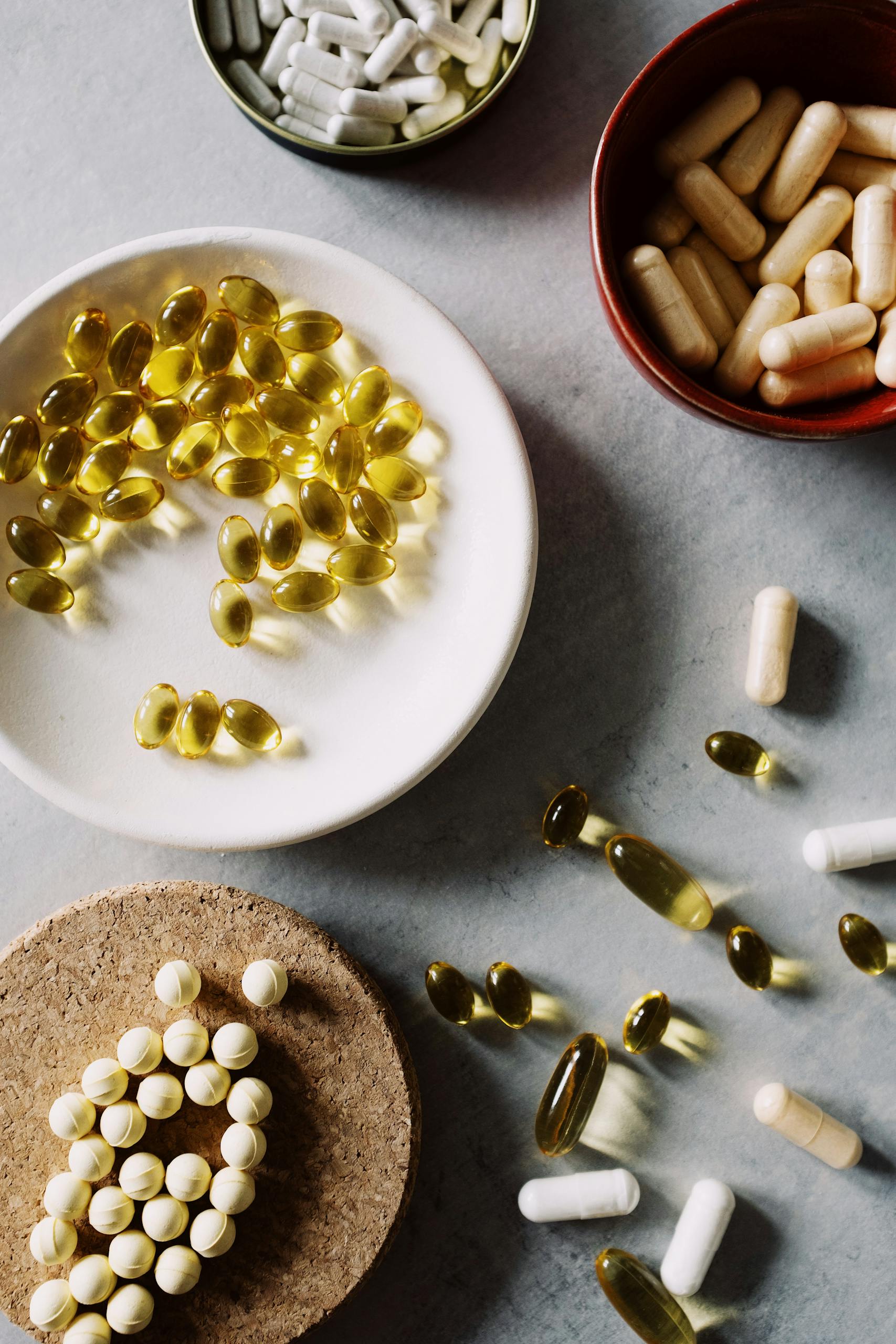 do you need vitamin D supplements: Top view of various pills and capsules in bowls on a marble surface, highlighting healthcare themes.