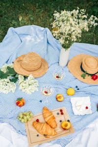 staying healthy while traveling: A beautiful summer picnic setup with croissants, fruits, wine, and straw hats on a blanket.