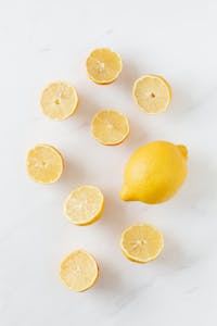 immune-boosting foods: A flat lay of whole and sliced fresh lemons on a clean marble surface.