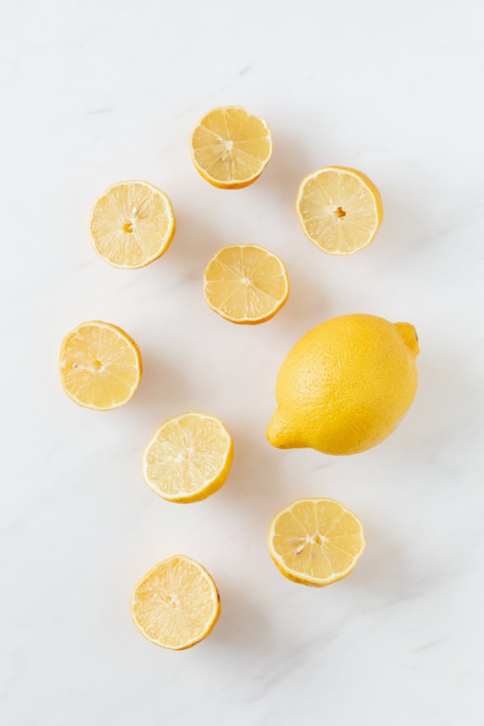 immune-boosting foods: A flat lay of whole and sliced fresh lemons on a clean marble surface.
