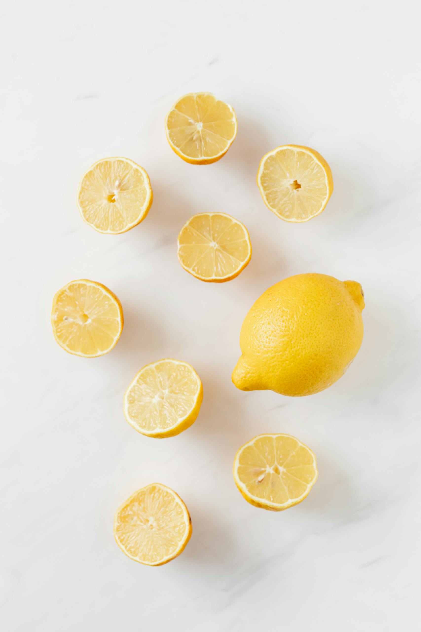 immune-boosting foods: A flat lay of whole and sliced fresh lemons on a clean marble surface.