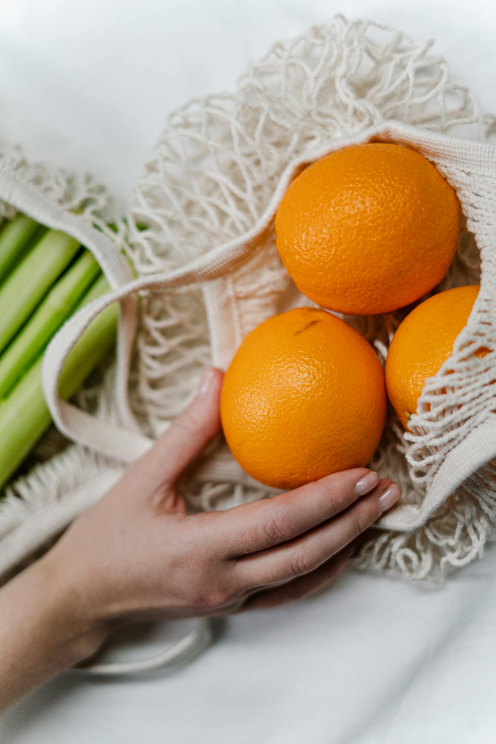 grocery shopping tips: A hand places oranges into a reusable mesh bag, emphasizing sustainable grocery shopping.