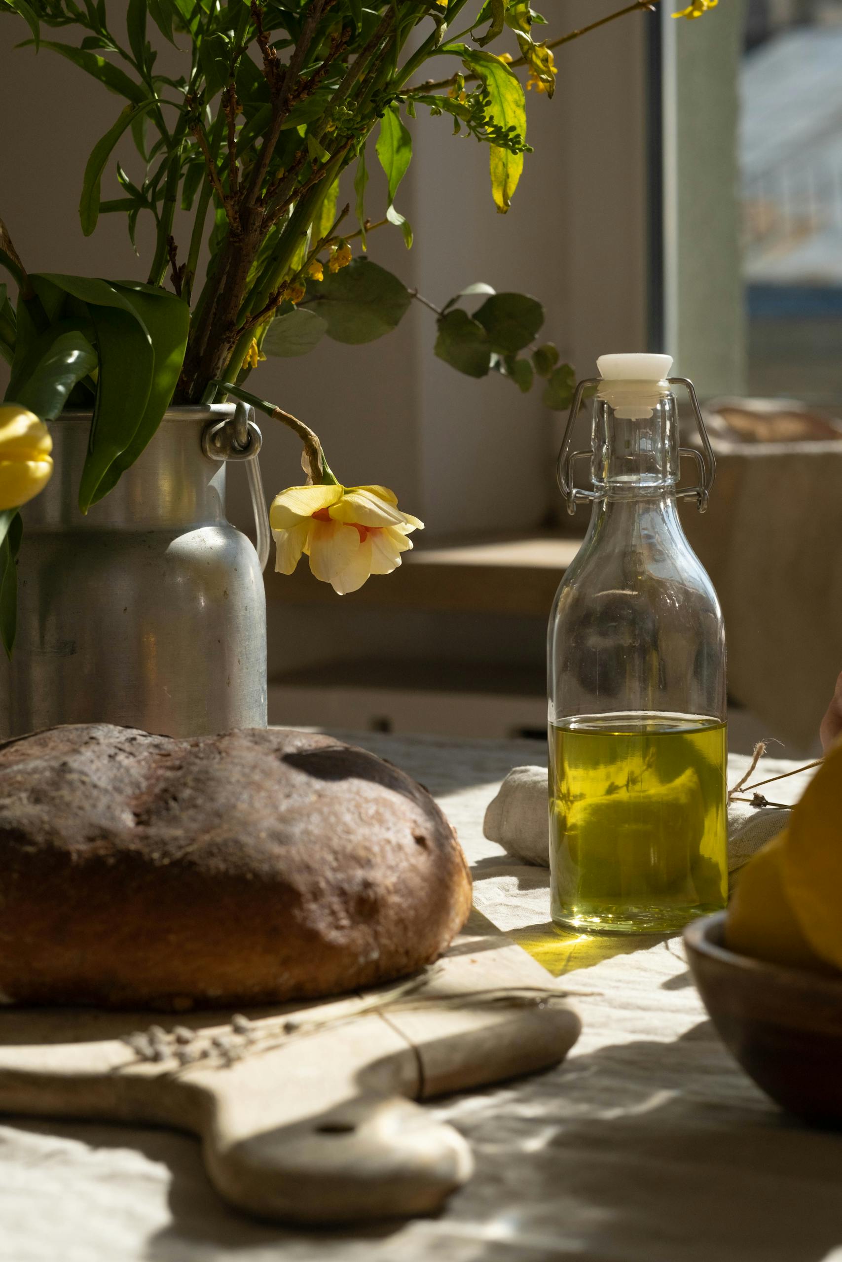 healthy fats: A serene kitchen setup featuring fresh bread, olive oil and flowers on a wooden table.