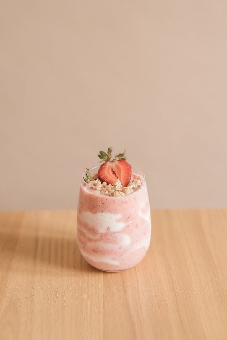 kefir benefits: Delicious strawberry smoothie with granola topping in a glass on a wooden table.