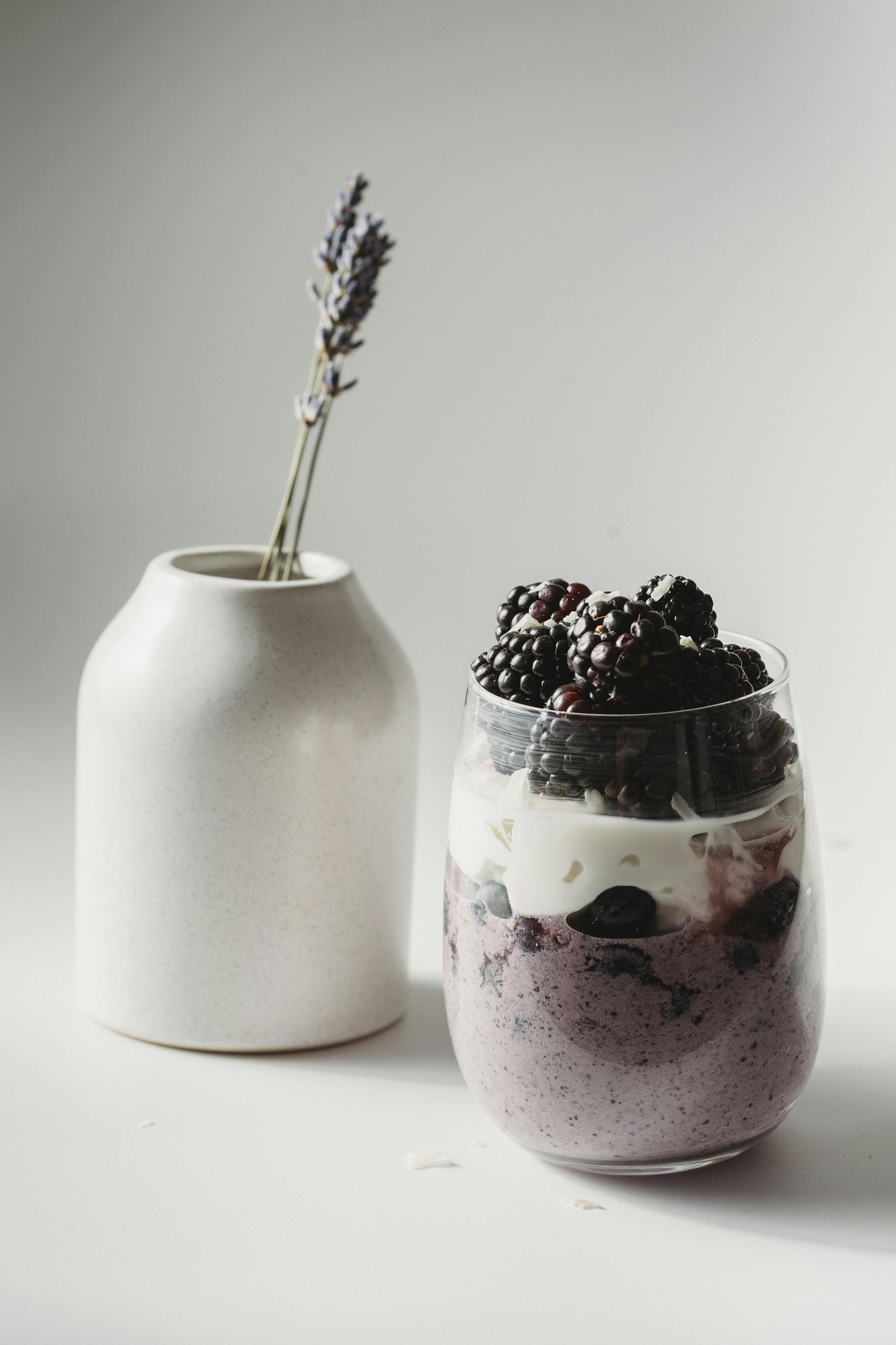 instant pot yogurt: Elegant blackberry yogurt parfait with lavender vase on a minimalist background.