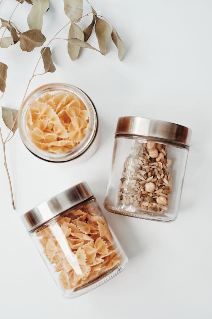 healthy pantry staples: Elegant display of farfalle pasta and seeds in glass jars on a modern surface.