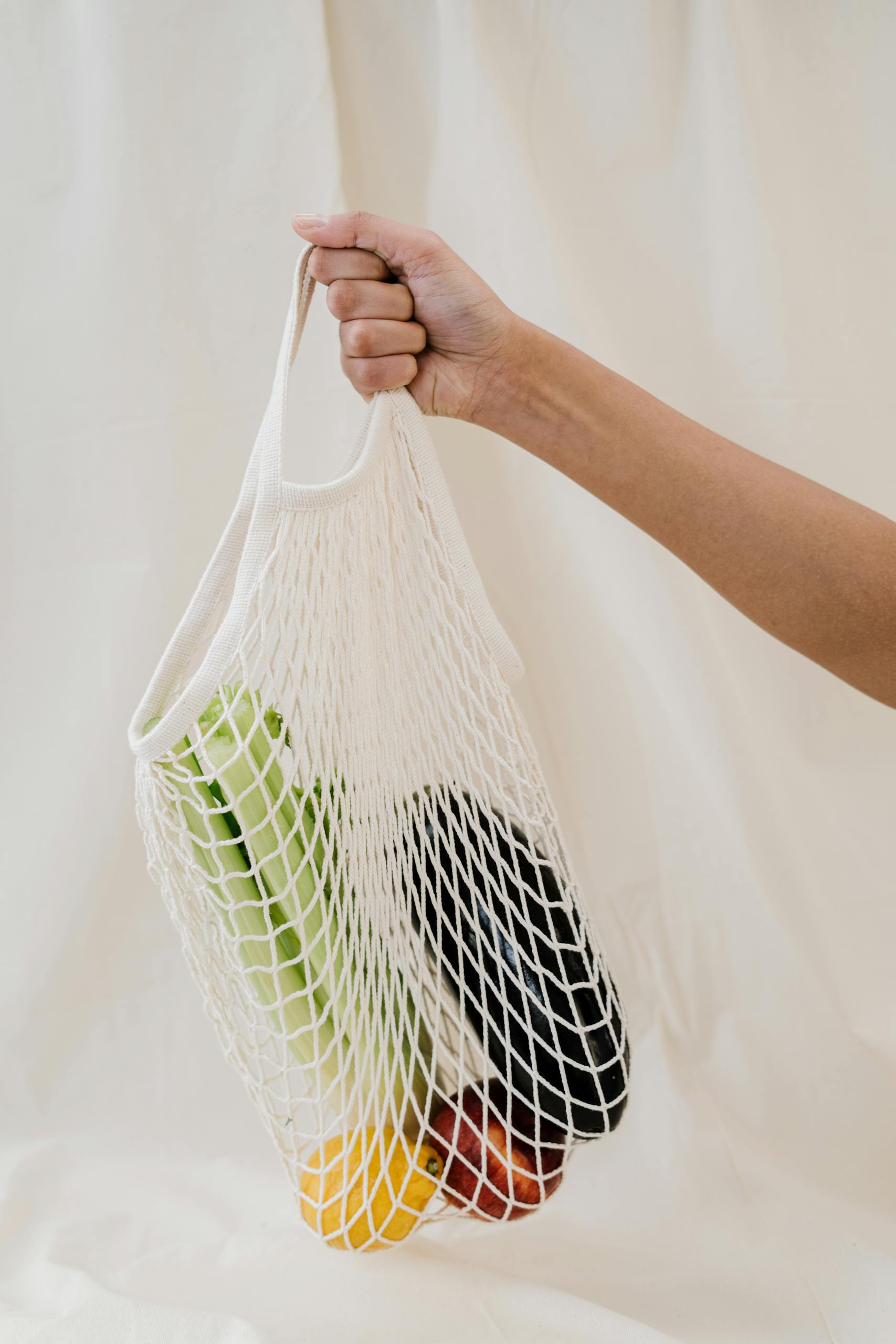 grocery shopping tips: Hand holding a reusable mesh bag filled with colorful fresh vegetables, promoting zero waste lifestyle.