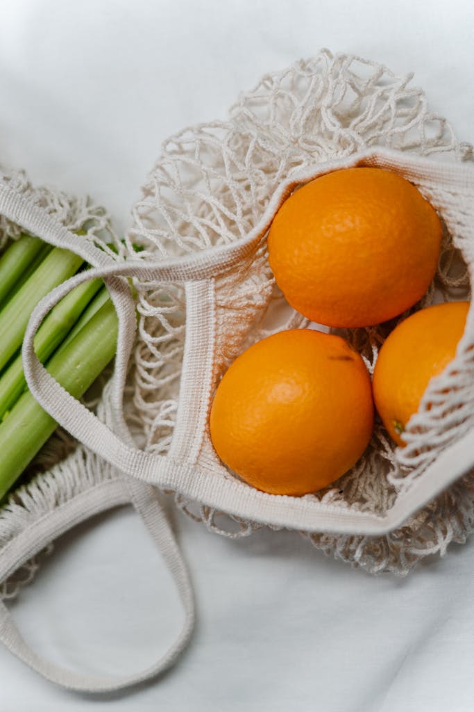 immune-boosting foods: Mesh bags containing fresh oranges and celery stalks, promoting zero waste and eco-friendly living.