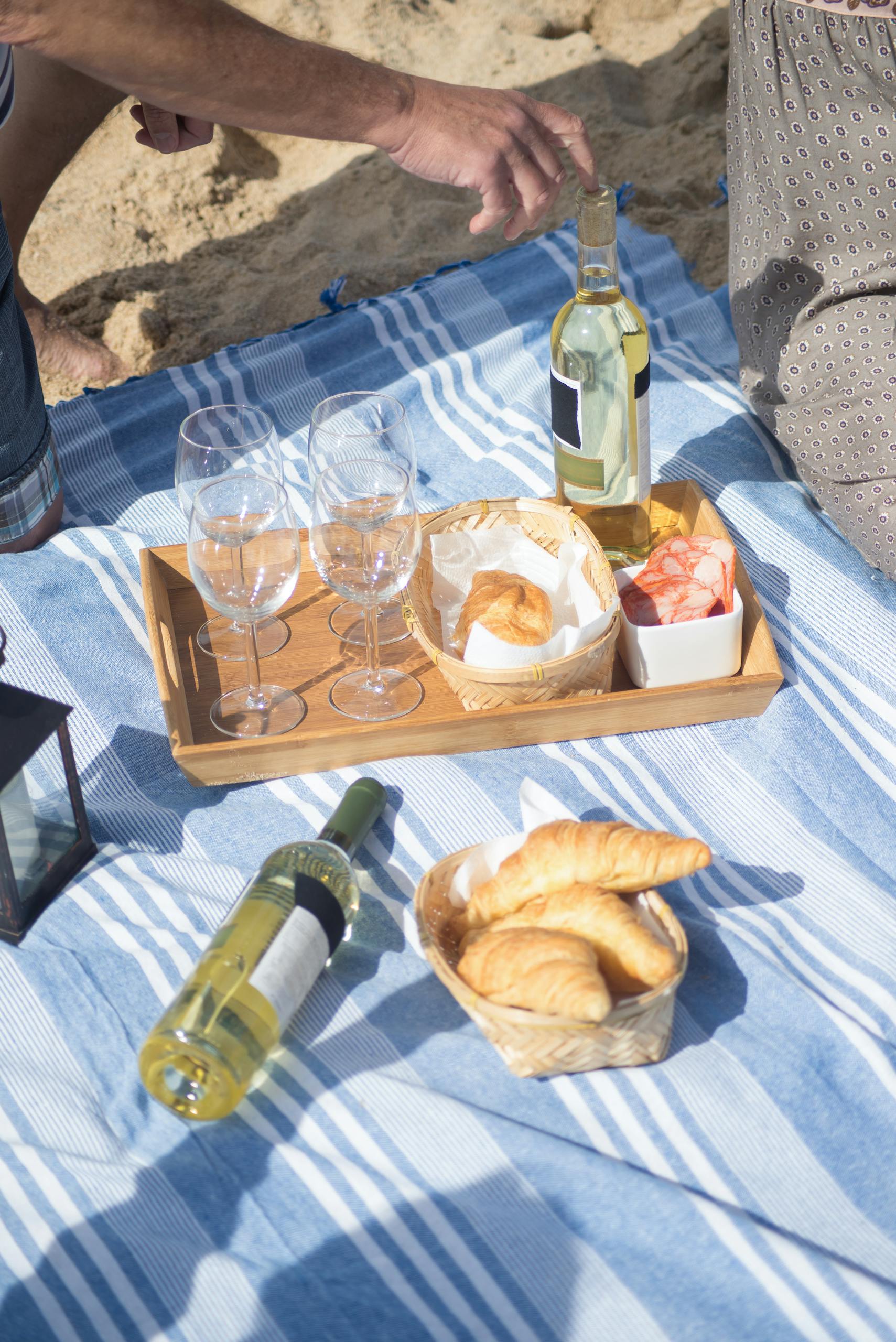 staying healthy while traveling: Relaxing beach picnic scene with wine, pastries, and a wooden tray on a striped blanket in Portugal.