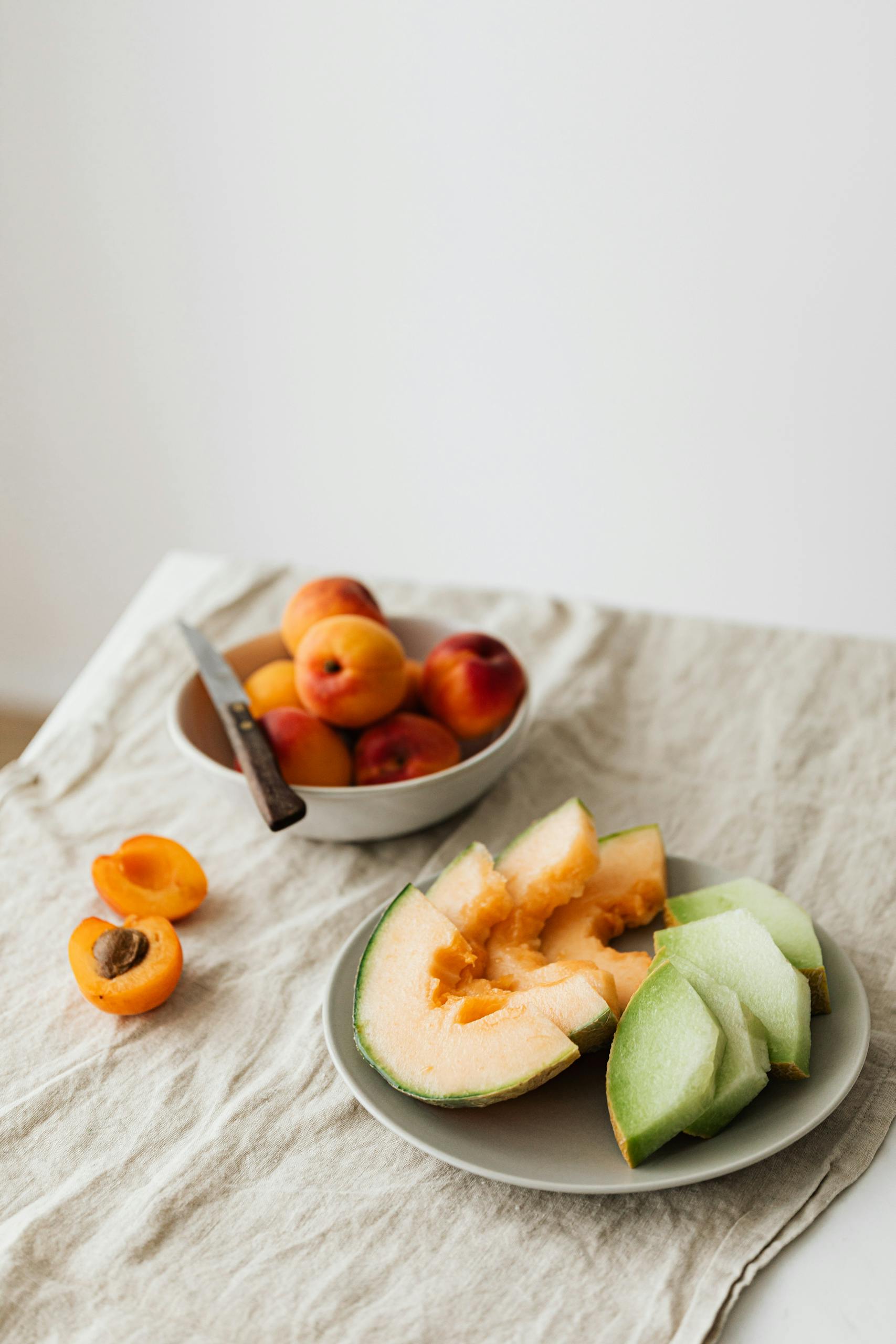 starvation mode: Still life of delicious healthy assorted melons on plate and bowl with fresh ripe apricots placed on linen tablecloth