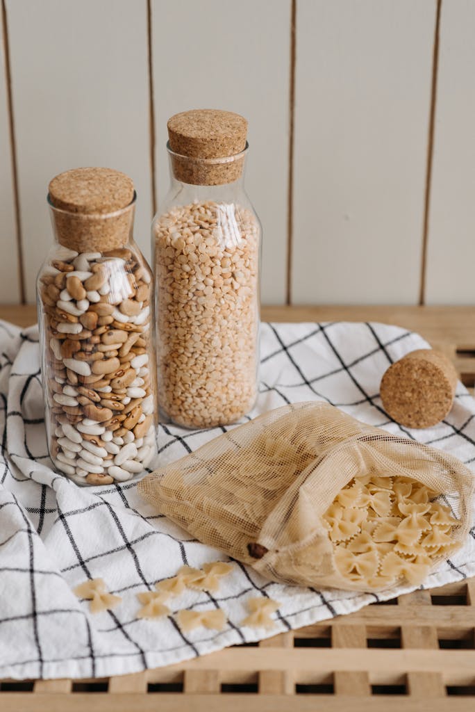 healthy pantry staples: Stylish pantry setup featuring glass jars with cork lids and a mesh bag with pasta on a wooden surface.