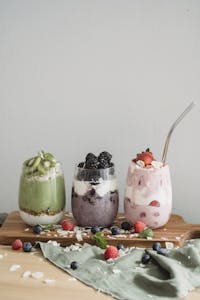 instant pot yogurt: Three colorful fruit smoothies with yogurt and berries on a wooden board, perfect for a healthy snack.