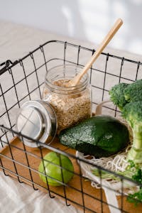 grocery shopping tips: Wire basket with avocado, lime, broccoli, and oatmeal in a glass jar.