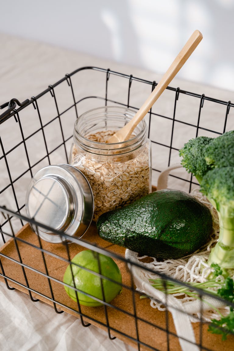 grocery shopping tips: Wire basket with avocado, lime, broccoli, and oatmeal in a glass jar.