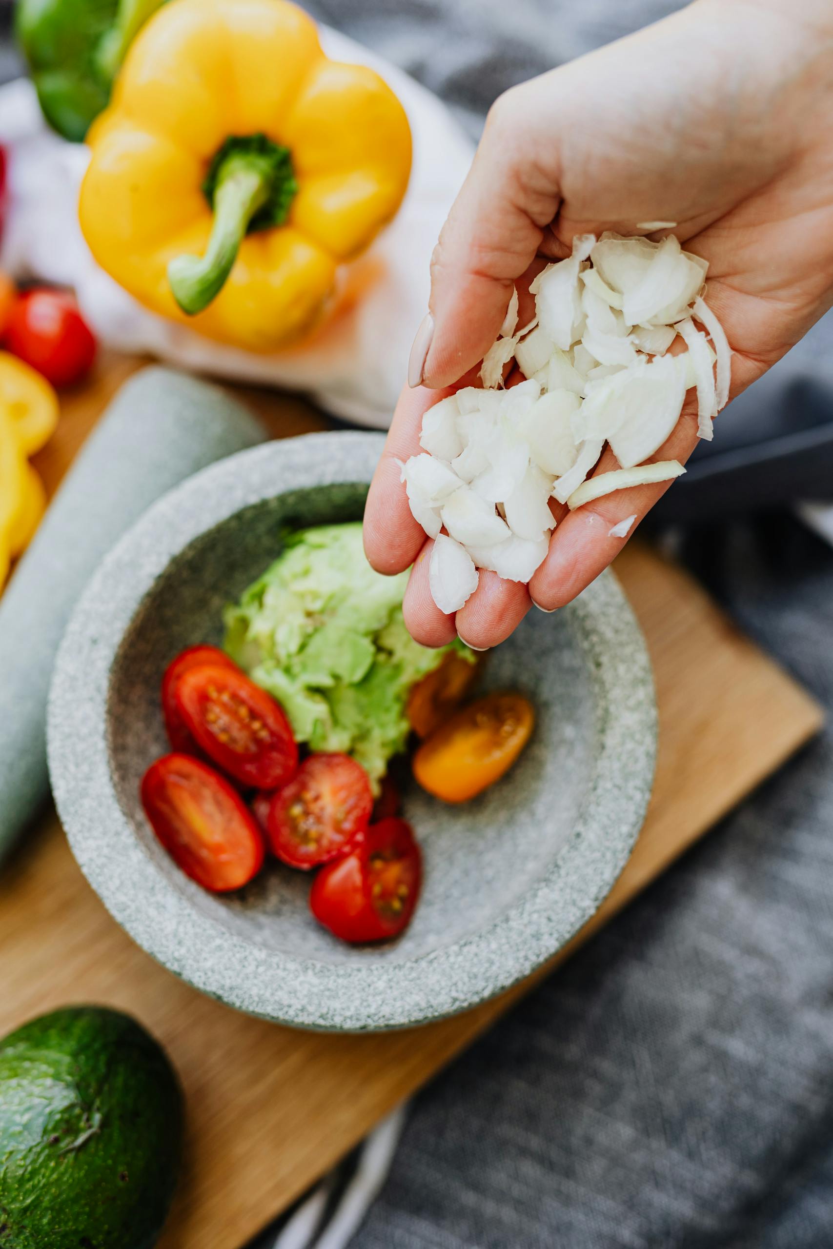 tips for vegetarians: Hand adding onions to guacamole with tomatoes and peppers in a molcajete, top view.
