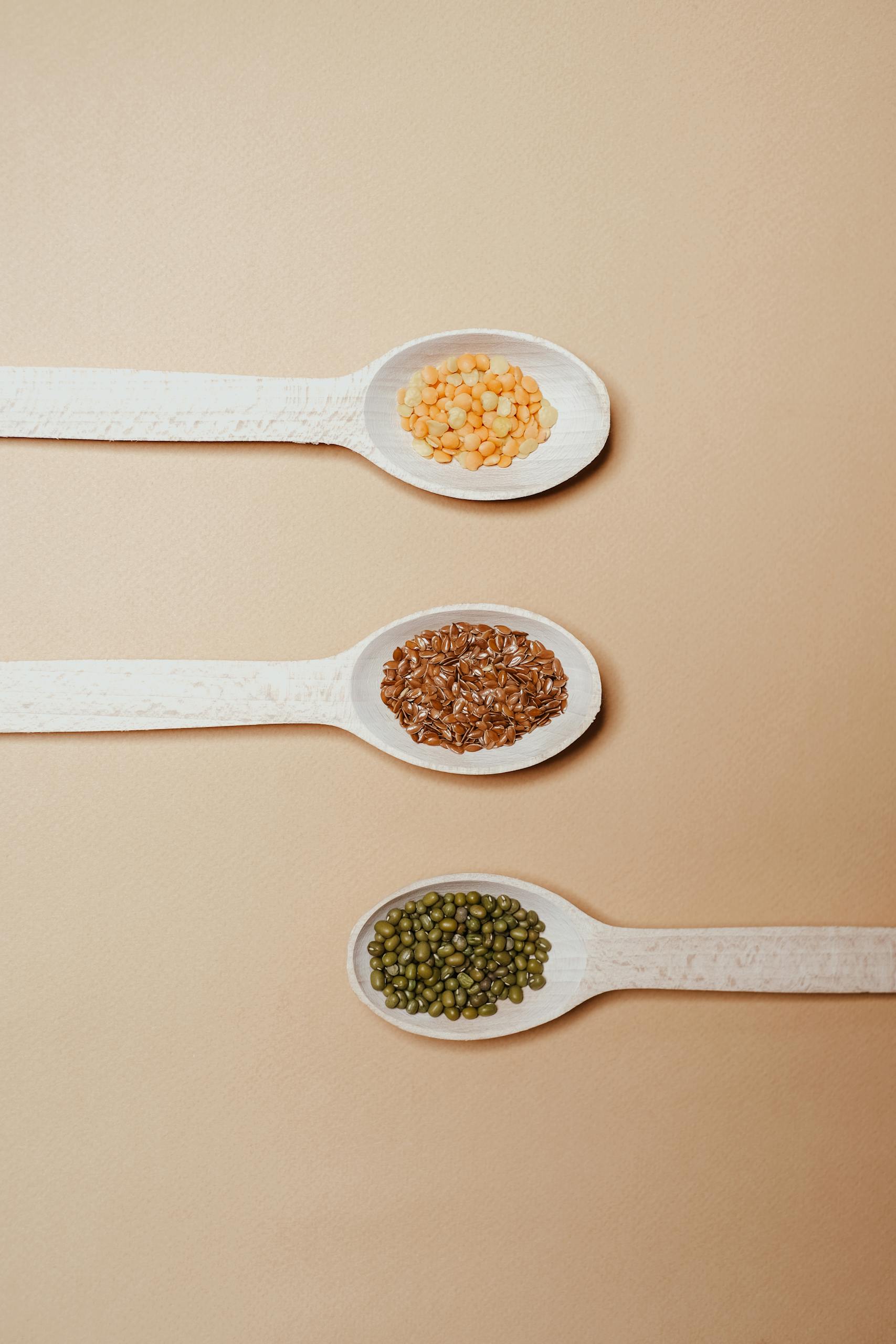 Close-up of various grains in white wooden spoons on a soft brown background, showcasing nutrition.