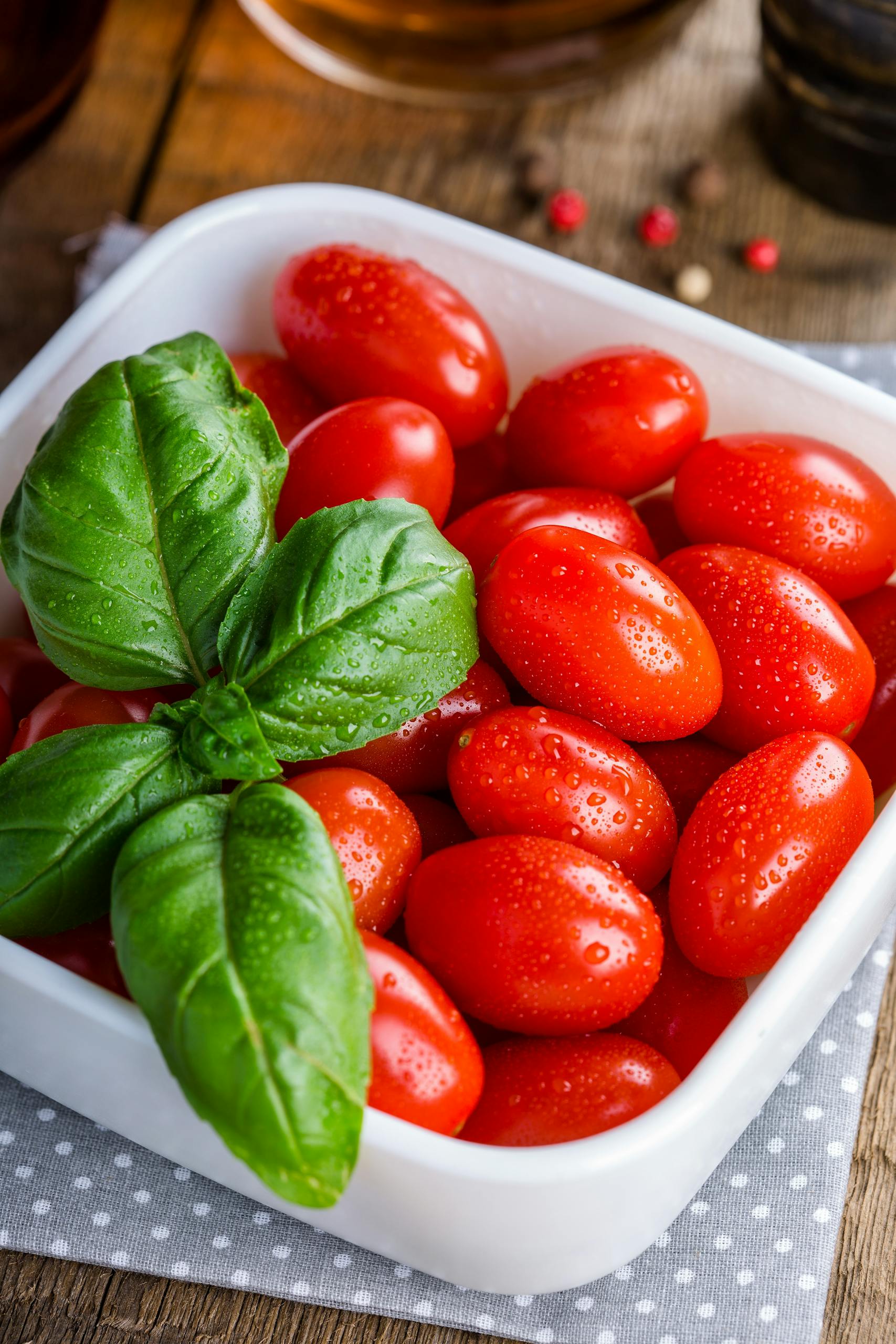 healthier alternatives to keto: A bowl of vibrant cherry tomatoes garnished with fresh basil leaves on wooden background.