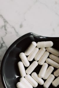 best probiotics for digestion: A close-up view of white capsules in a black bowl on a marble surface, emphasizing medicine and health.