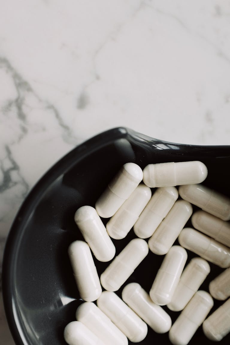 best probiotics for digestion: A close-up view of white capsules in a black bowl on a marble surface, emphasizing medicine and health.