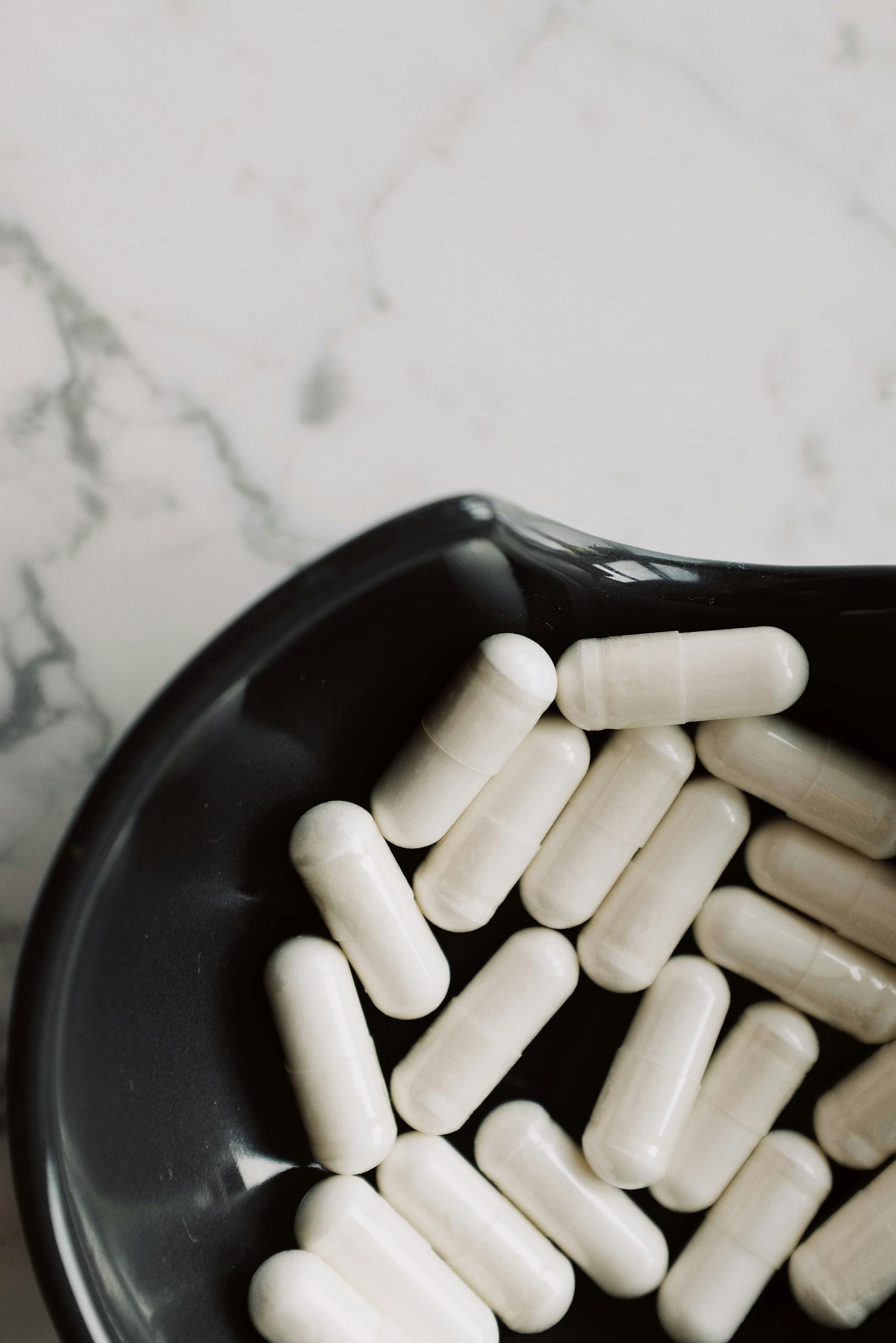 best probiotics for digestion: A close-up view of white capsules in a black bowl on a marble surface, emphasizing medicine and health.