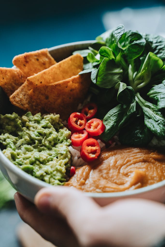 easy ways to add magnesium-rich foods to your diet: A colorful vegan buddha bowl featuring guacamole, veggies, and tortilla chips.
