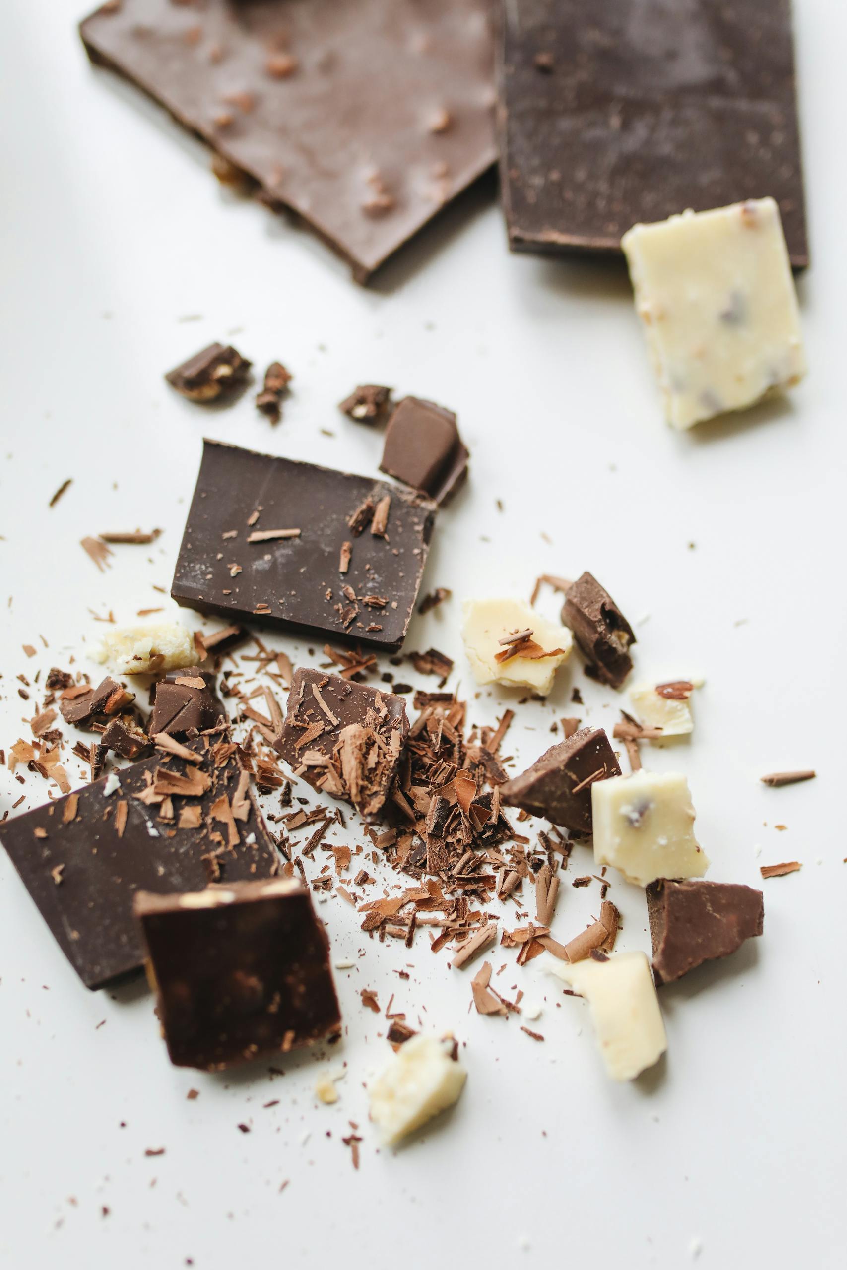 easy ways to add magnesium-rich foods to your diet: A delicious assortment of broken chocolate pieces on a white background with a focus on dark and white chocolate.